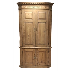  Georgian pine corner cupboard, projecting dentil cornice over blind fretwork frieze, the top section with canted fluted corners enclosed by two panelled doors, green painted interior with three shaped shelves, the bottom section with two panelled doors, on plinth base, W122cm, H218cm  