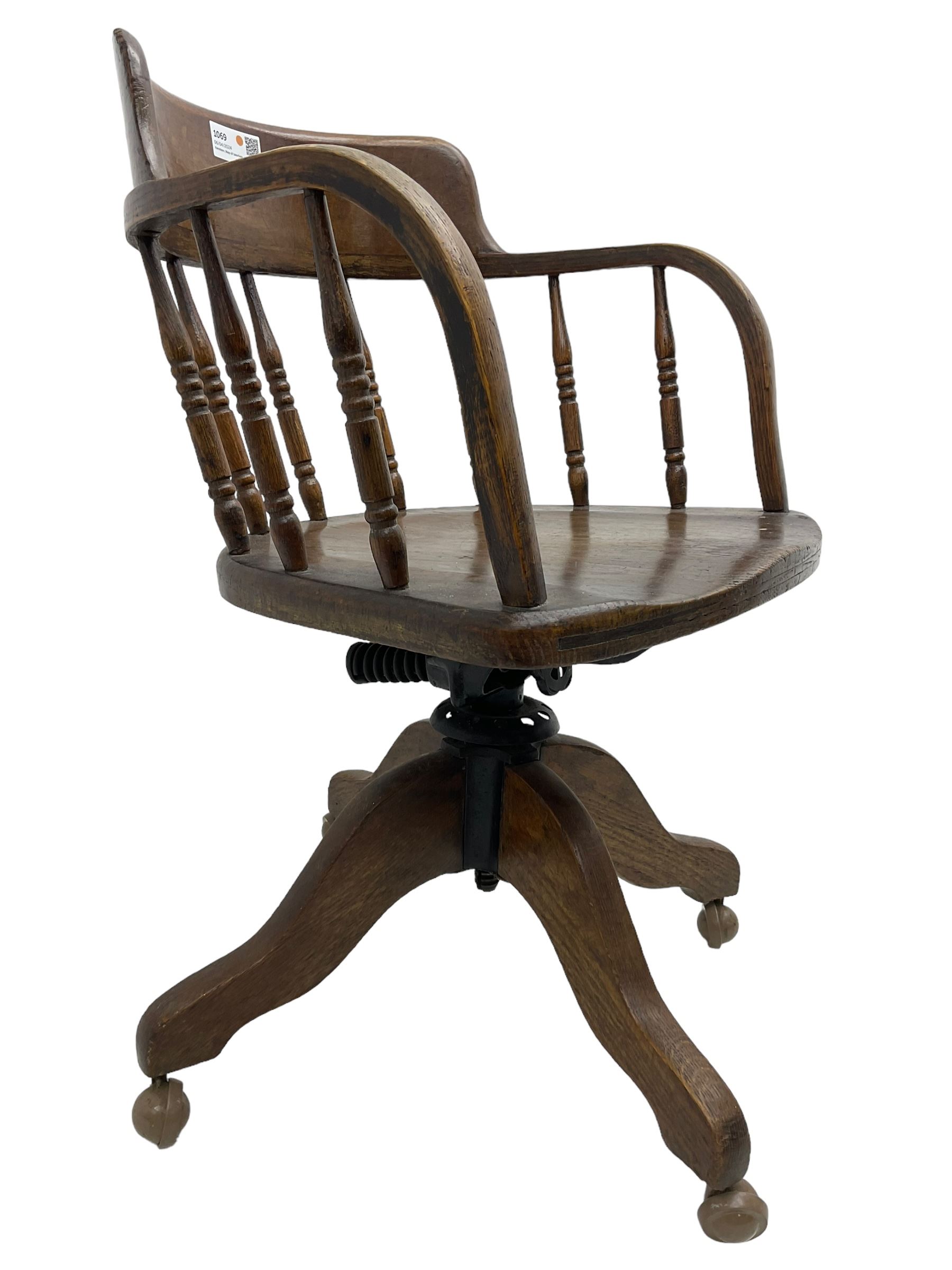 Early 20th century oak framed swivel Captain's chair, tub shaped back with turned spindle supports over saddle shaped seat, quadriform base on castors