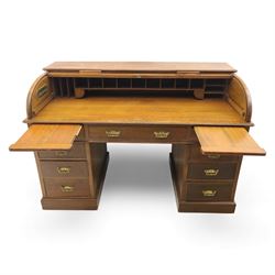 Edwardian oak roll-top desk, the tambour enclosing a fitted interior of pigeonholes and dividers, over a central kneehole flanked by twin banks of drawers with brass handles, on plinth bases