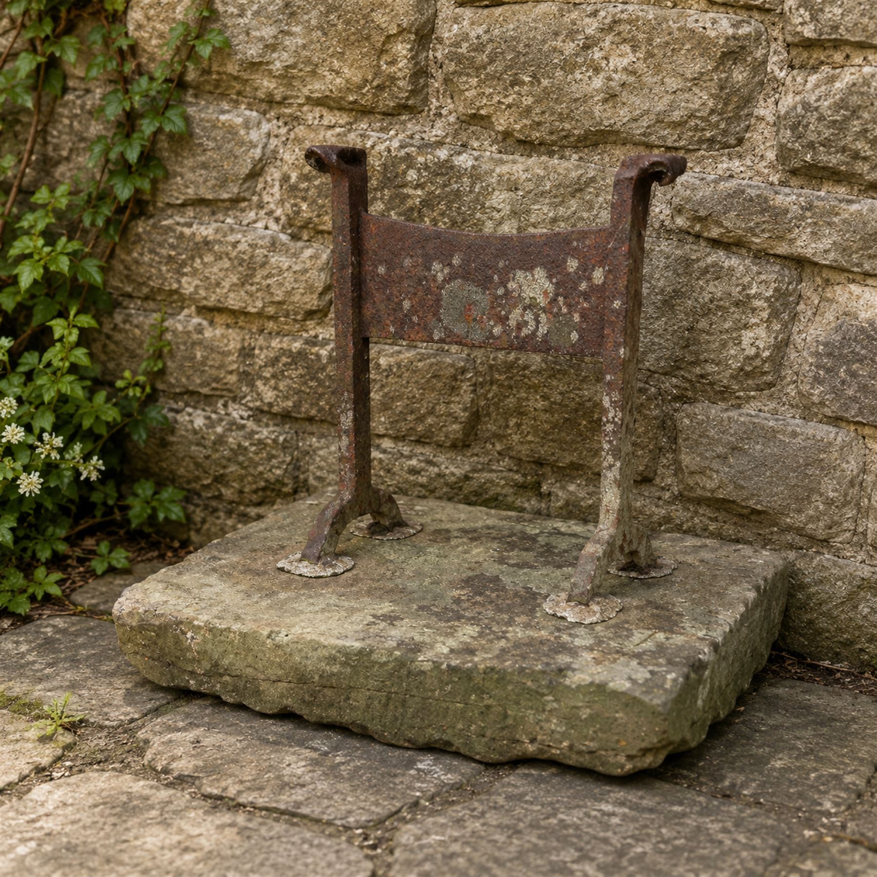 19th century cast iron boot scraper, mounted on a rectangular hewn stone slab base, with scrolled twin upright supports and scraper bar, in weathered finish