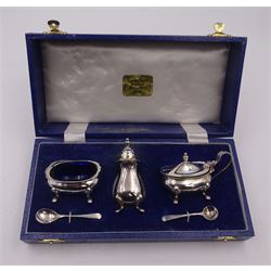Modern three piece silver cruet set, comprising pepper shaker, open salt, mustard pot and cover, all of typical form with shaped rims and upon four pad feet, the pepper shaker and mustard pot with urn shaped finials, together with two matching condiment spoons, all hallmarked Turner & Simpson Ltd, Birmingham 1978, the mustard pot and salt with blue glass liners, all within fitted case