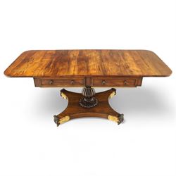 Regency rosewood sofa table, rectangular top with variegated rosewood veneers, hinged D-shaped leaves, over a set of dummy drawers to the back and full-size drawers to the front, with turned knob handles and gilt beaded moulding on frieze above elegant turned, tapering, and fluted, pedestal with a well-carved collar, supported on a large, tripartite concave platform base terminating in richly carved lion paw feet with gilded acanthus leaf carving, on concealed brass castors, circa 1815, length extended 161cm 
