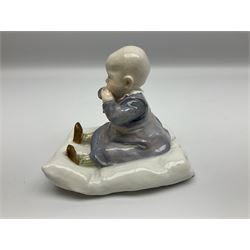 Early 20th century Meissen figure, circa 1905-1924, designed by Konrad Hentschel, modelled as a baby seated upon a cushion wearing a merging purple and blue dress, green and white striped leggings and brown shoes, with blue crossed swords mark and incised model number U 150 beneath, H12.5cm

