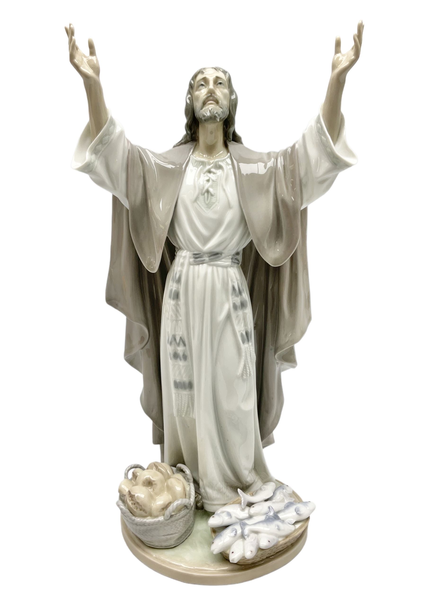 Lladro figure, The Loaves and Fishes, modelled as Jesus Christ with arms raised standing beside a basket of loaves and a basket of fish, sculpted by Salvador Furió, with original box, no 5896, year issued 1992, year retired 1997, H35cm