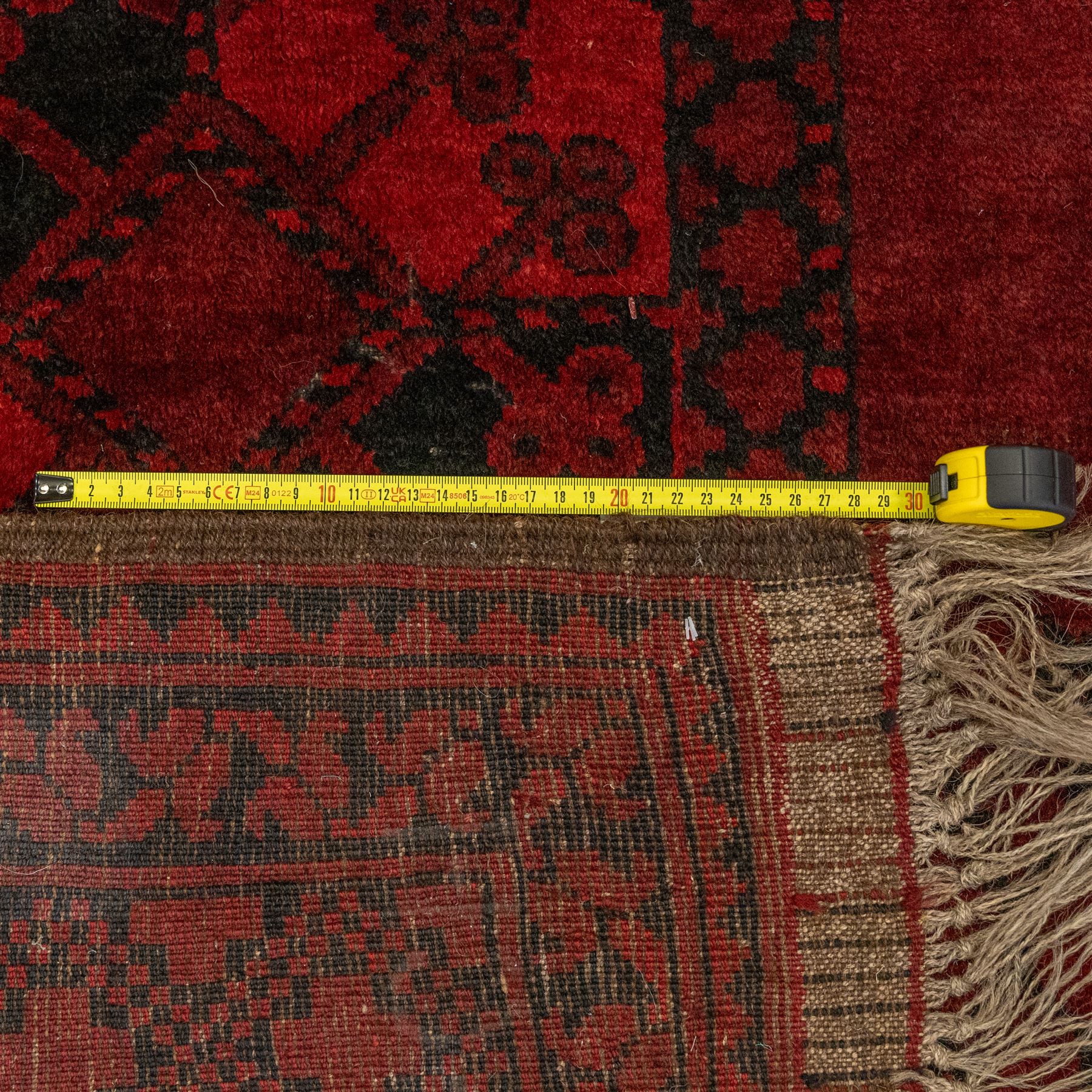 Turkmen Bokhara carpet, with a deep red field and repeating rows of black gul motifs, within multiple geometric borders