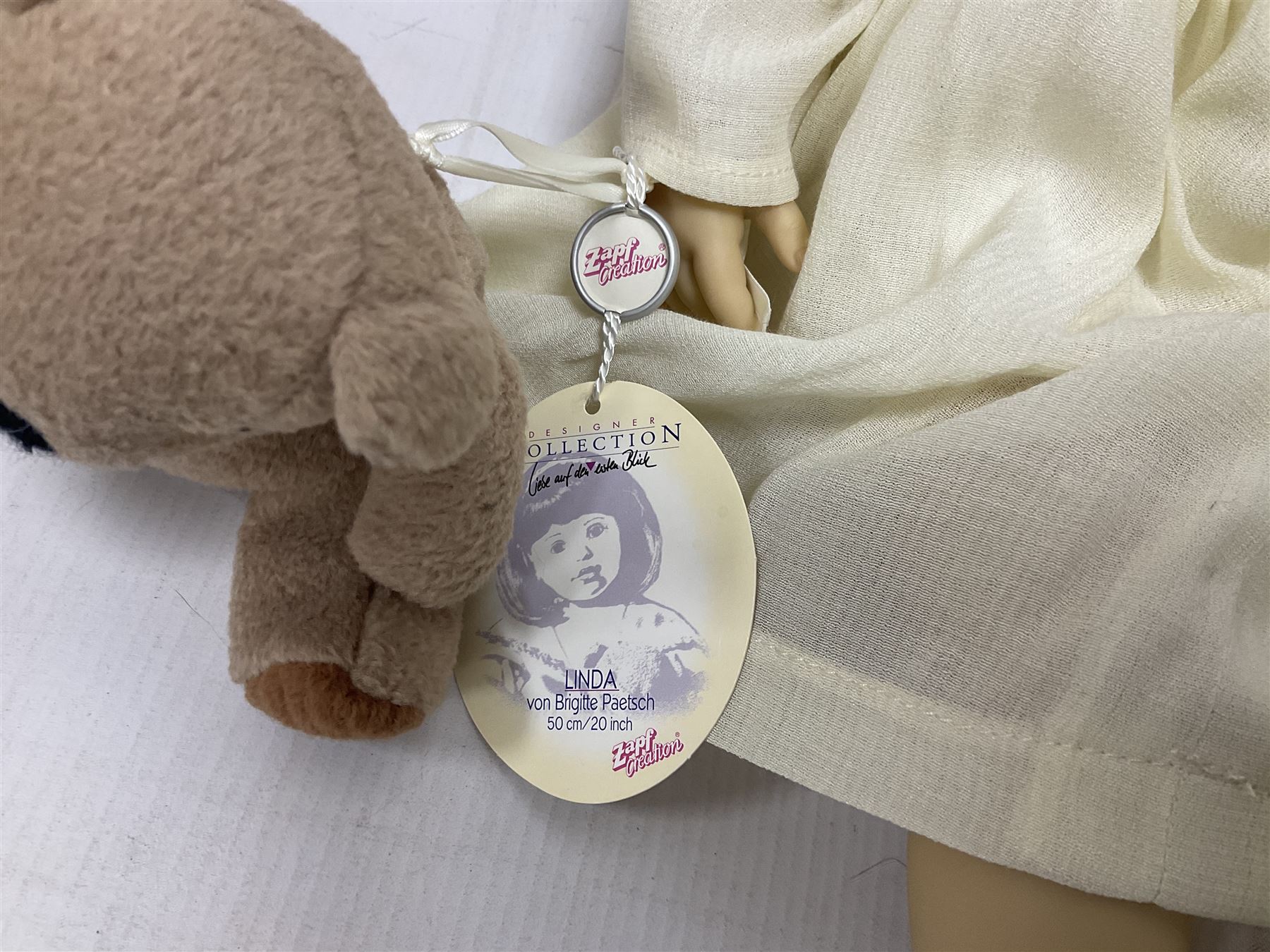 Two Zapf Creation limited edition designer collection dolls, by Brigette Paetsch, the first example with faux suede jacket, red jumper and denim skirt, no. 460, the second example 'Linda' in white dress with teddy bear accessory, no. 785, each signed B Paetsch, tallest L60cm