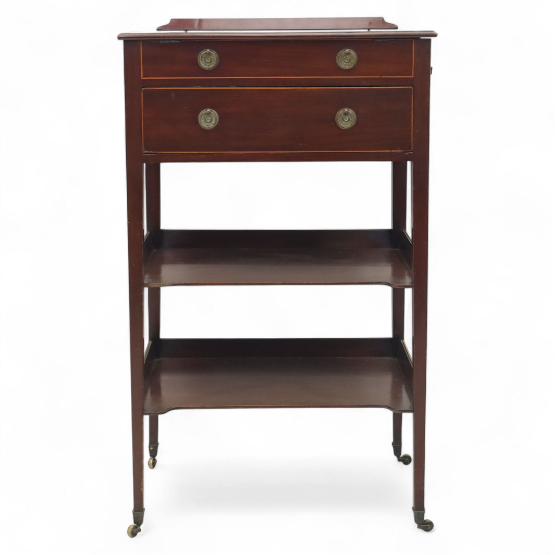 George III mahogany and boxwood-strung drawing table, the rectangular sloping reading surface with rest and oak stay, above a blind drawer and a drawer fitted with brass ring handles, side with pull-out candleholder and inkwell compartment, raised on square-section tapered legs with brass box castors united by two galleried under tiers