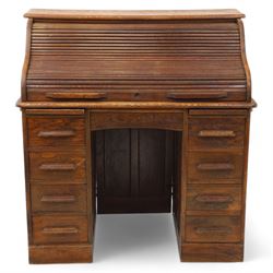 Early 20th-century oak roll-top desk with tambour shutter, enclosing a fitted interior of pigeon holes and small drawers, and pedestal base fitted with nine drawers with moulded handles, raised on plinth base 