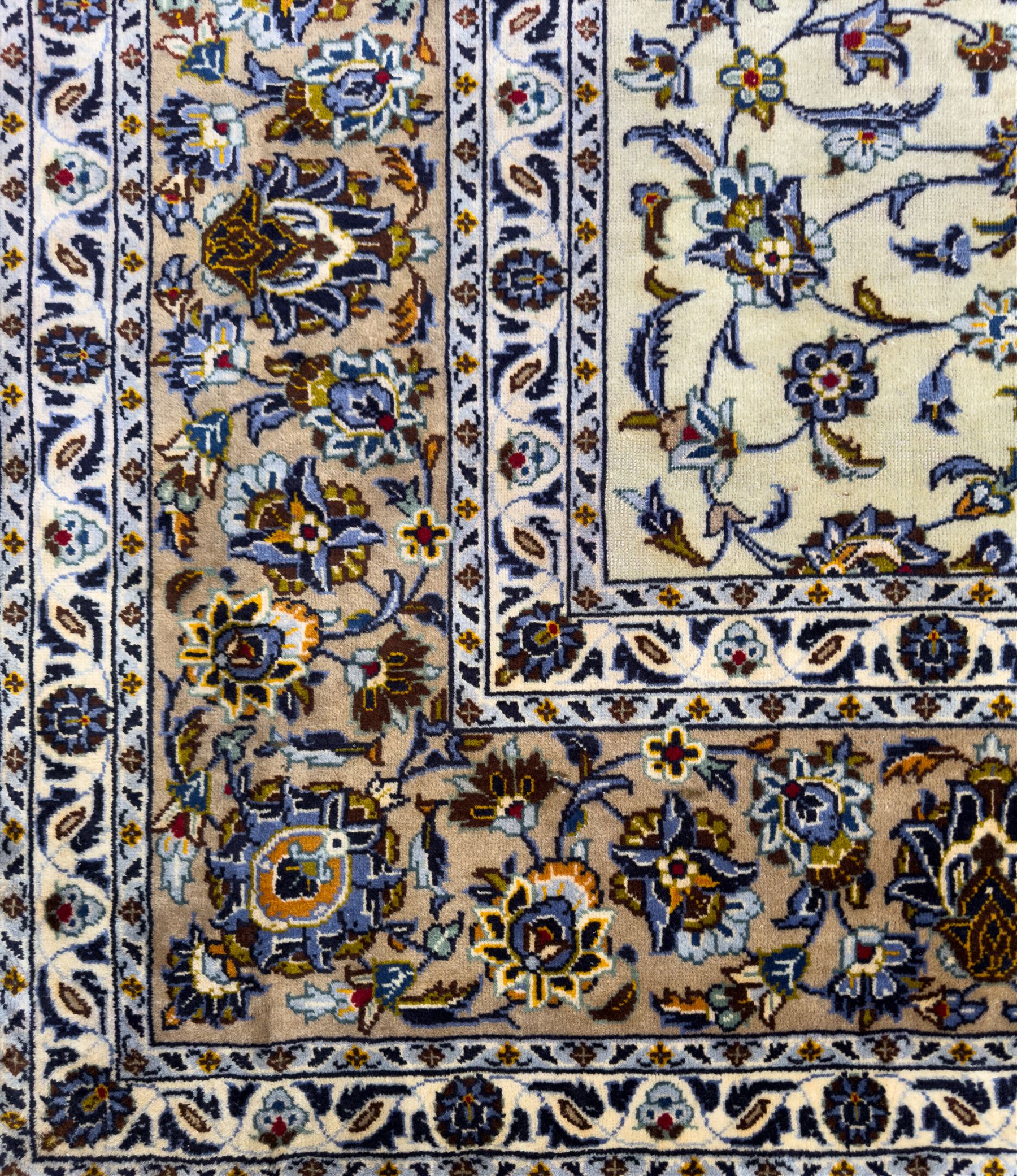 Central Persian Kashan hand-knotted carpet, ivory field with an all-over design of scrolling vines, lotus palmettes, and rosettes in shades of blue, gold, and brown within a blue ground border of palmettes and arabesques between multiple guard stripes