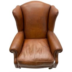Georgian design wingback armchair, upholstered in brown leather with stud band and piping, turned and fluted front feet on brass cups and castors