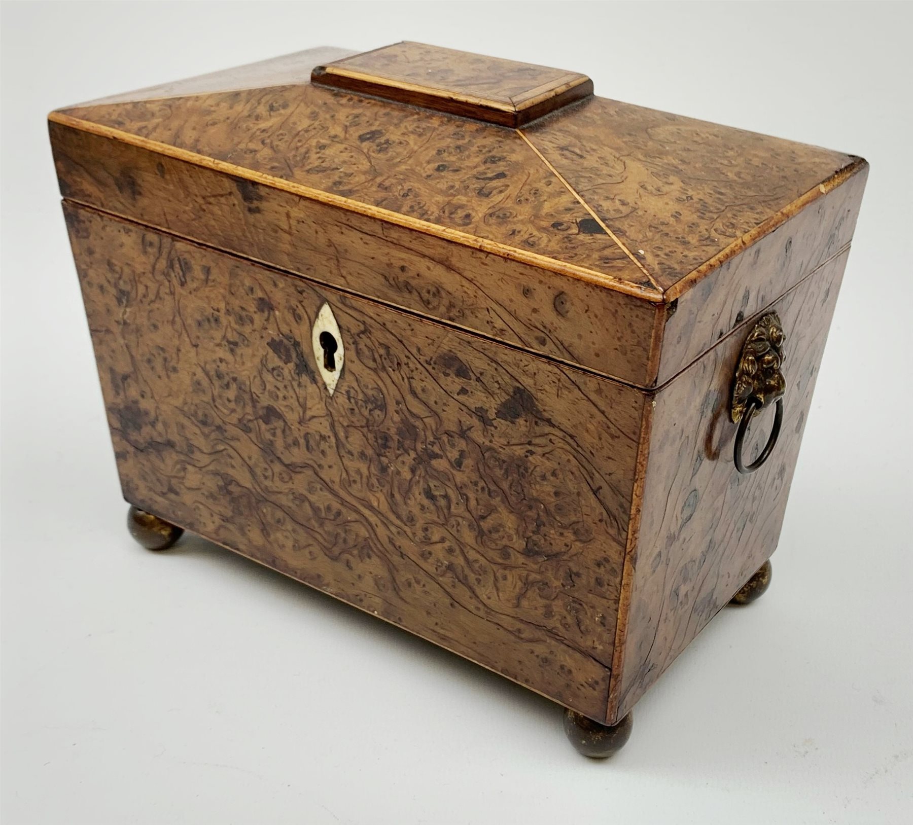 George III burr yew tea caddy, of sarcophagus form with lion mask ring handles and four brass ball feet, the hinged lid opening to reveal two compartments with cross-banded lids and traces of metallic paper lining, L19cm