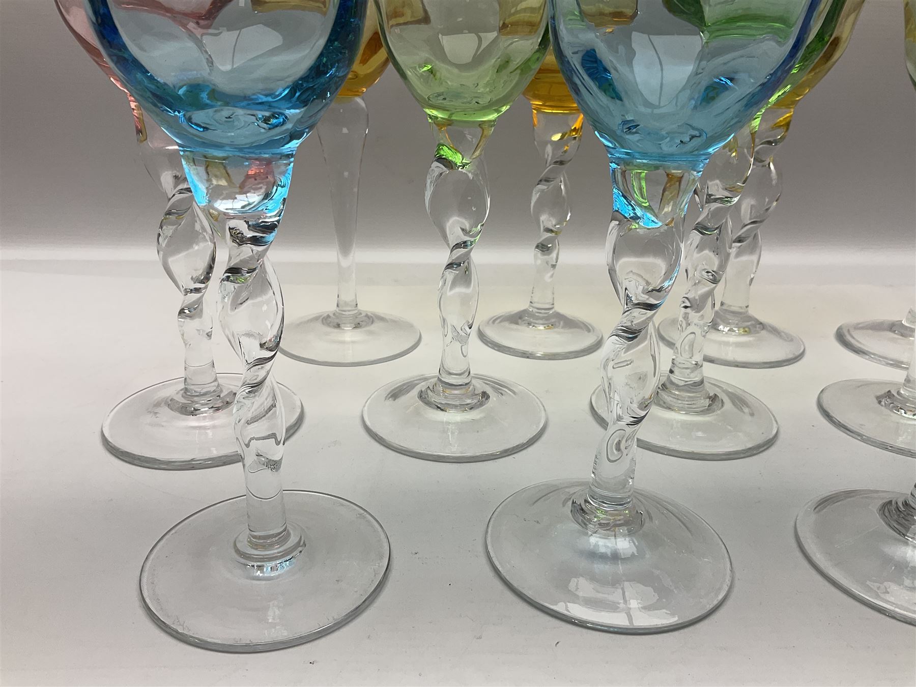Ten coloured Adriana wine glasses by Abigails, to include blue, green, pink and yellow examples, each with part faceted bowl and twist stems, together with two similar orange examples with pulled stems, H24cm