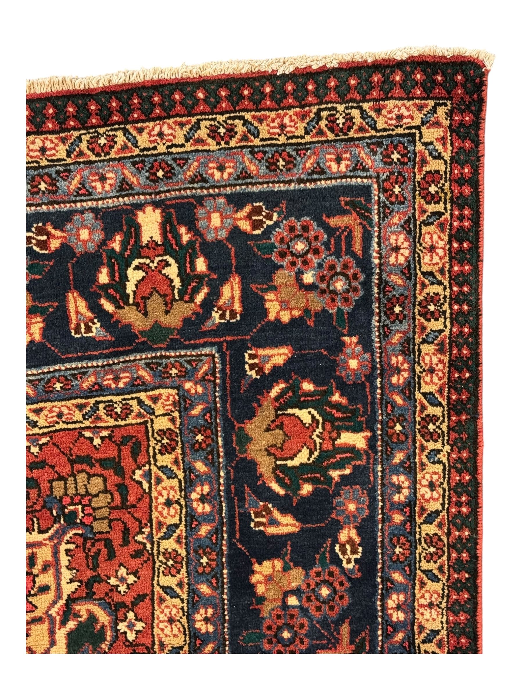 North East Persian Meshed crimson ground carpet, central indigo and green medallion with floral decoration, busy field with trailing foliage and stylised flowers, matching spandrels with floral motifs, indigo border featuring scrolling vines and palmettes, framed by narrow floral guard bands