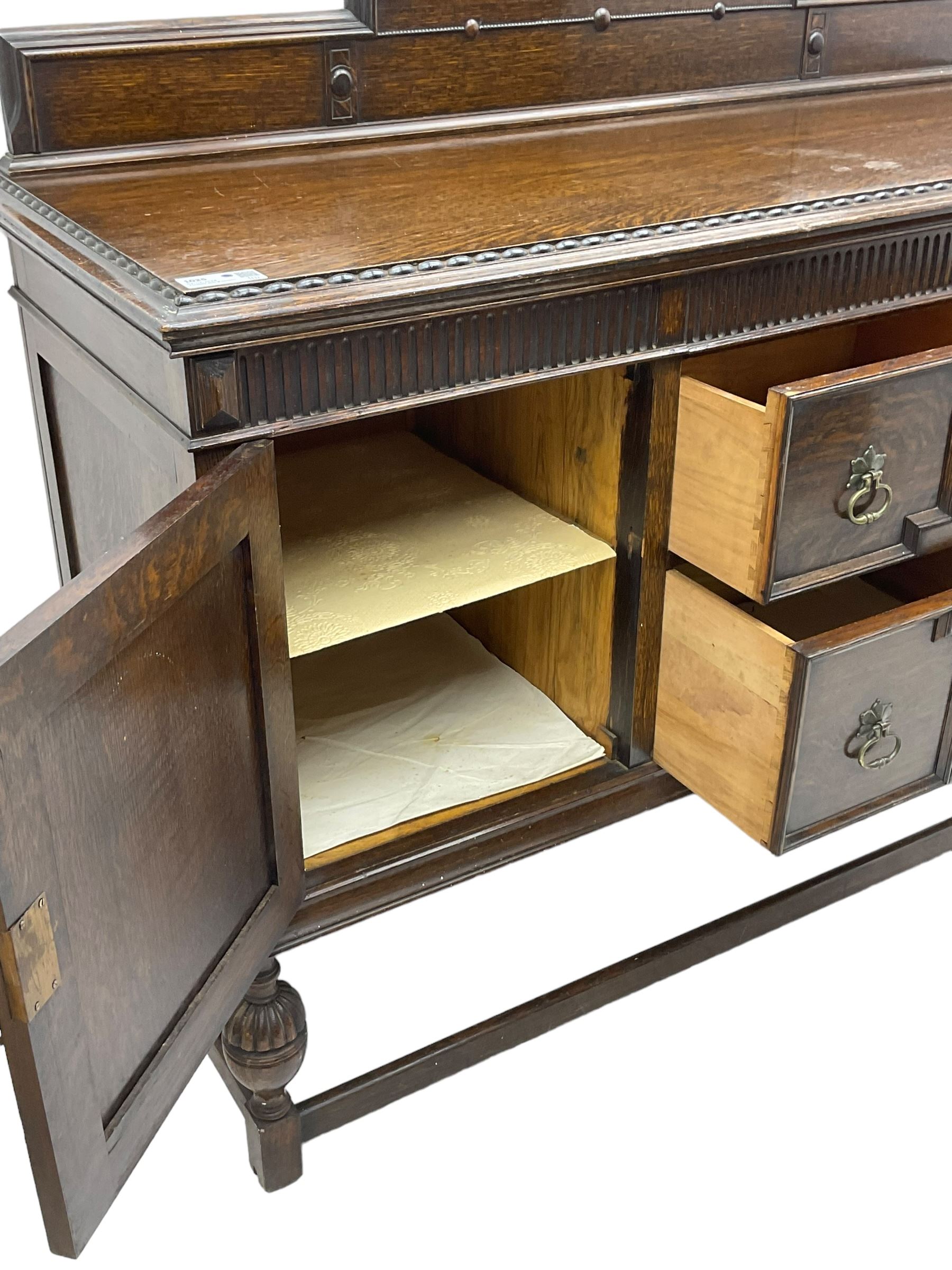 Early 20th century oak sideboard, raised stepped arch back over moulded rectangular top, fitted with two drawers and two panelled cupboards with geometric mouldings, on turned and lobe carved baluster feet united by stretchers 