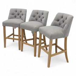 Contemporary set of three upholstered bar stools, each with button-tufted grey fabric backrest and seat, raised on light oak finish square legs united by stretchers