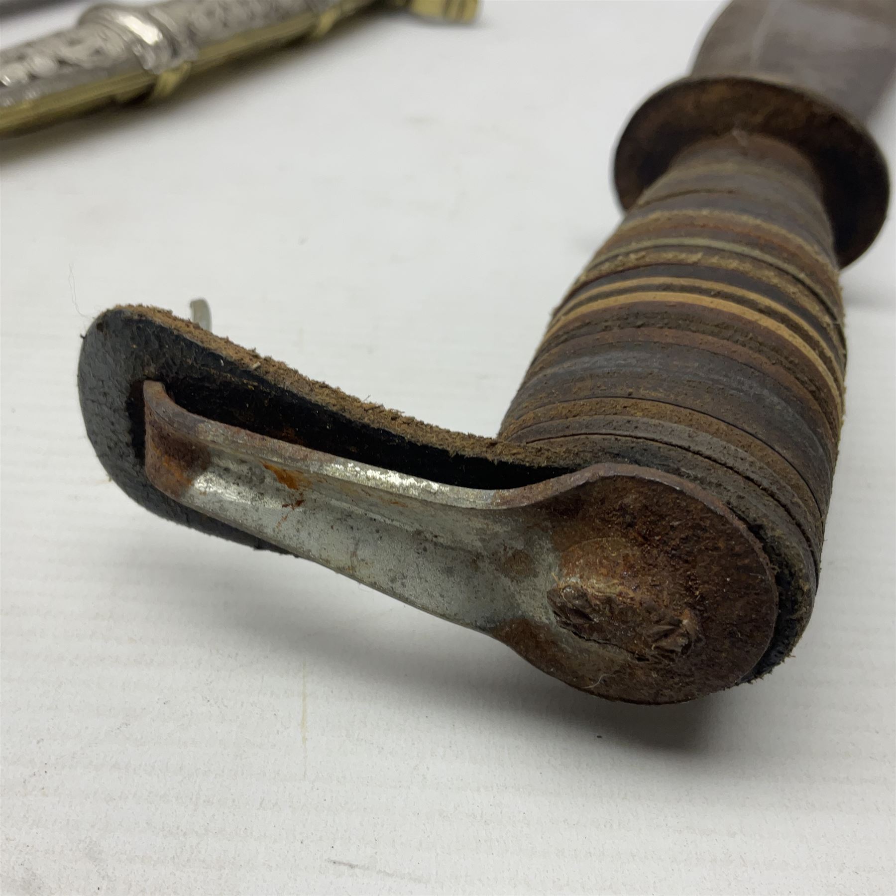 Moroccan jambiya dagger with 24.5cm plain curved blade stamped LONDON to the ricasso area, the hilt and scabbard overlaid with plain sheet brass to the back and ornate silver coloured metal to the front; waisted grip and arched pommel; two pyramid mounts to the scabbard L41cm overall; large billhook with curving blade and stacked leather washer grip; and a reproduction halberd blade (3)