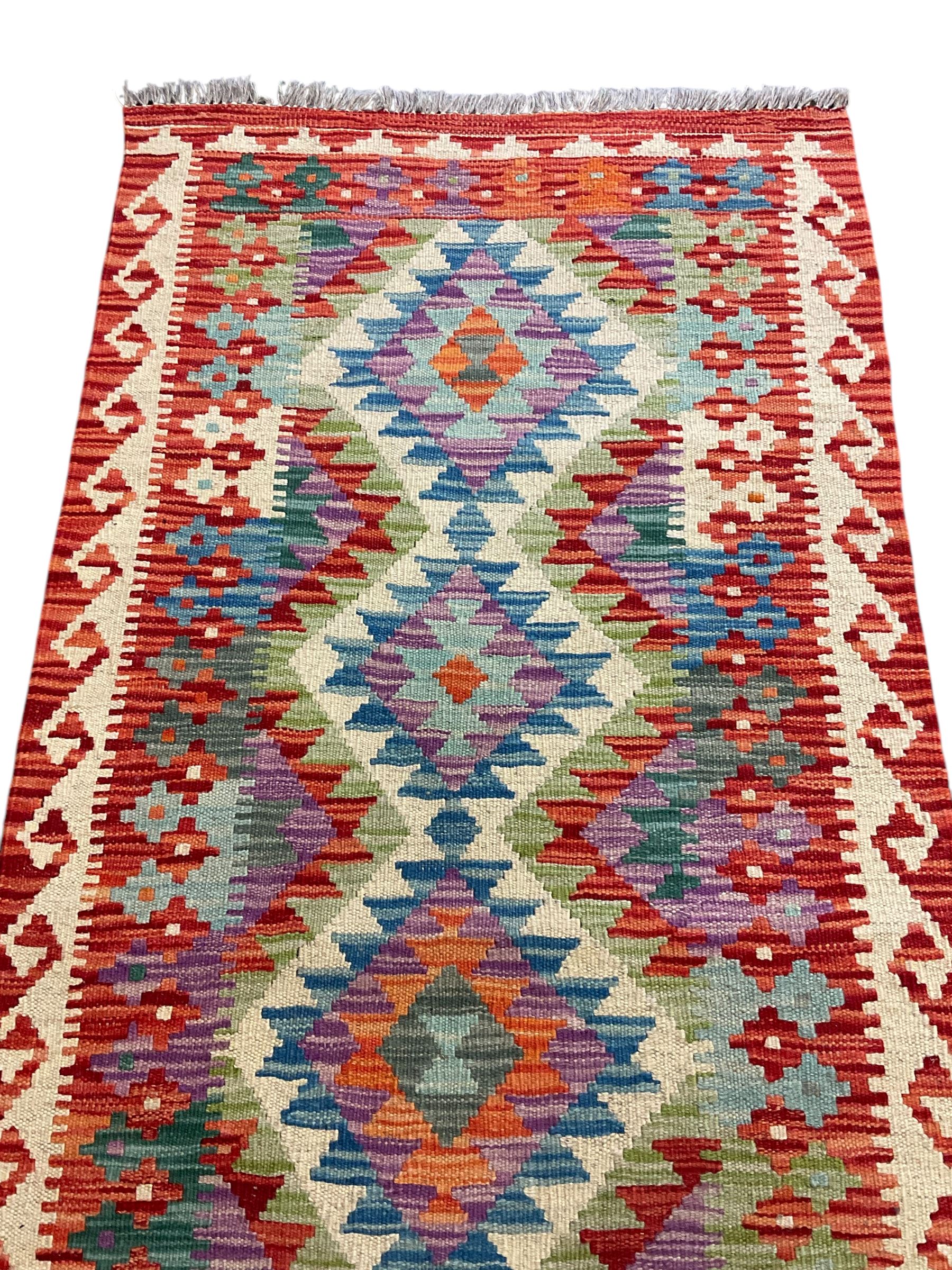 Chobi Kilim red ground and multi-coloured runner, decorated with overall geometric design, trailing lozenges within hooked border