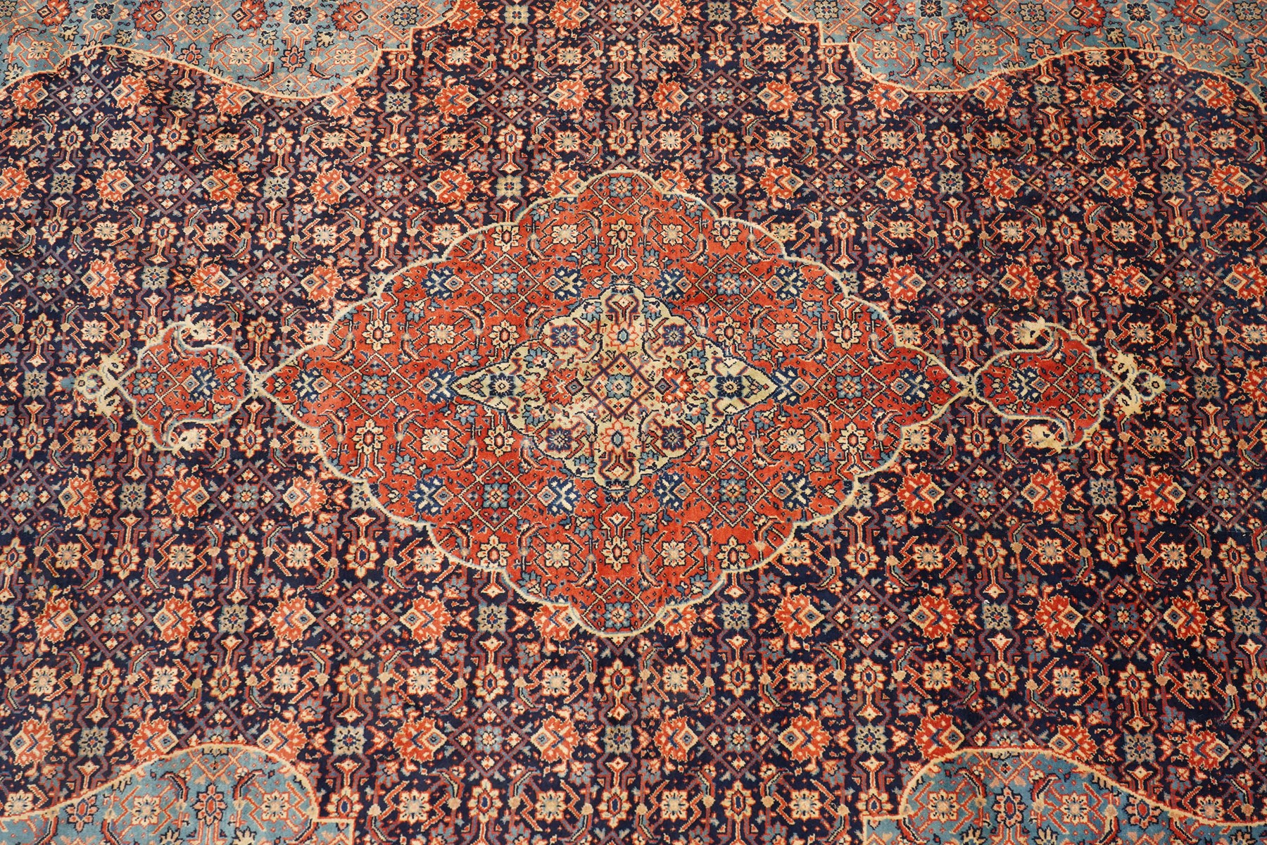 Persian indigo ground Herati rug, the busy field with a central lozenge pole medallion surrounded by repeating Herati motifs, within a shaped spandrel border the crimson guard band decorated with repeating palmette motifs
