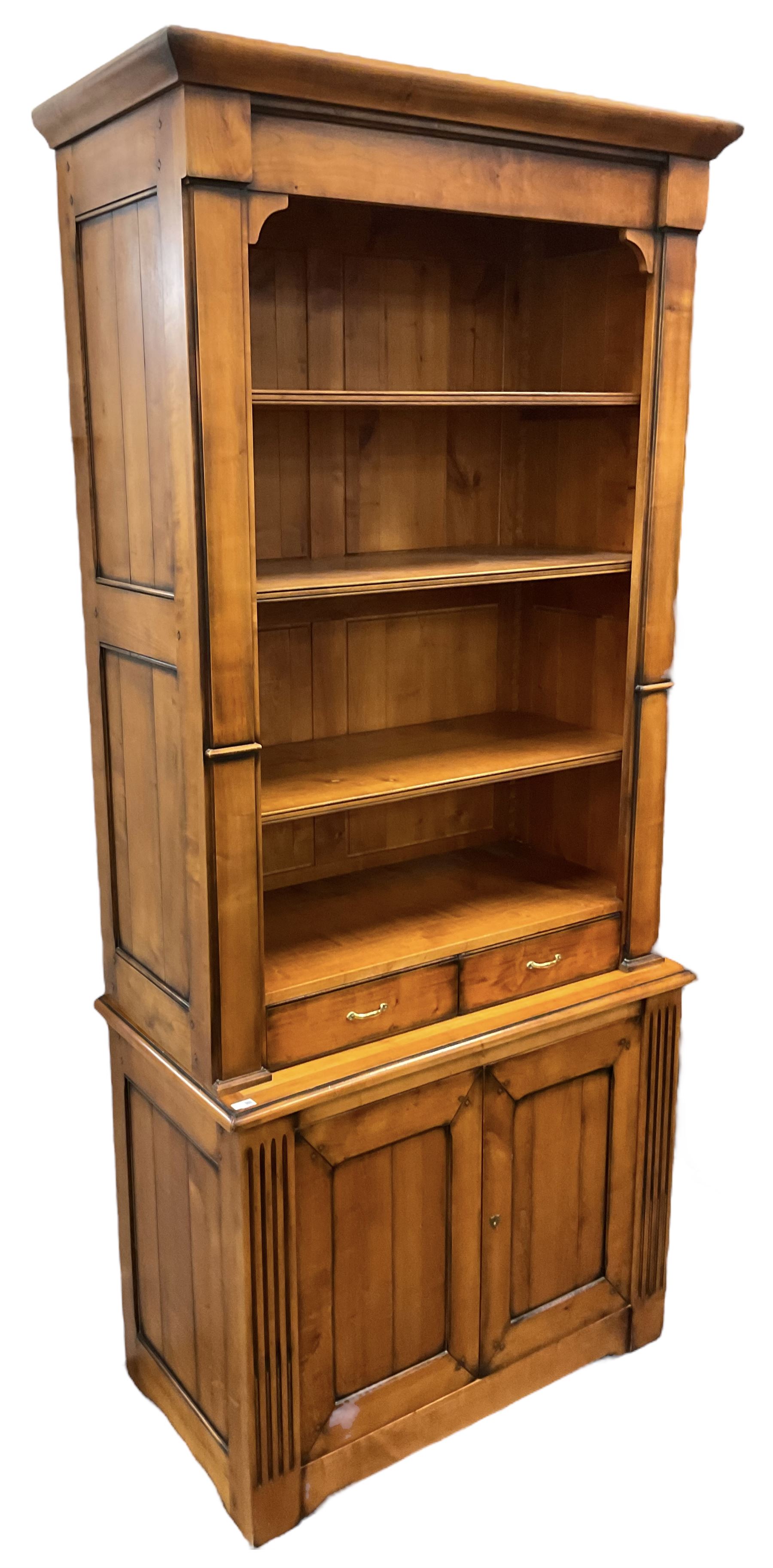 French cherry wood bookcase on cupboard, projecting moulded cornice over three shelves and two small drawers, the cupboard enclosed by two panelled doors flanked by fluted uprights