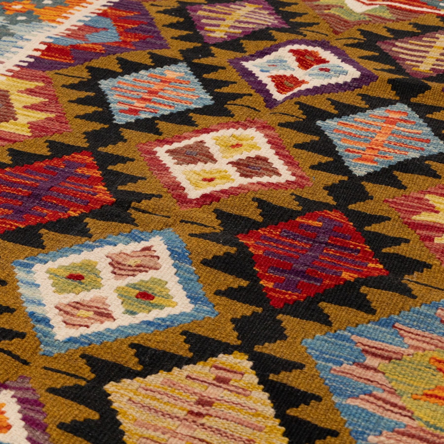 Afghan kilim rug, the field in earthy tones decorated with columns of repeating lozenges with further geometric motifs, the teal guard band with repeating stepped lozenges heightened with ivory