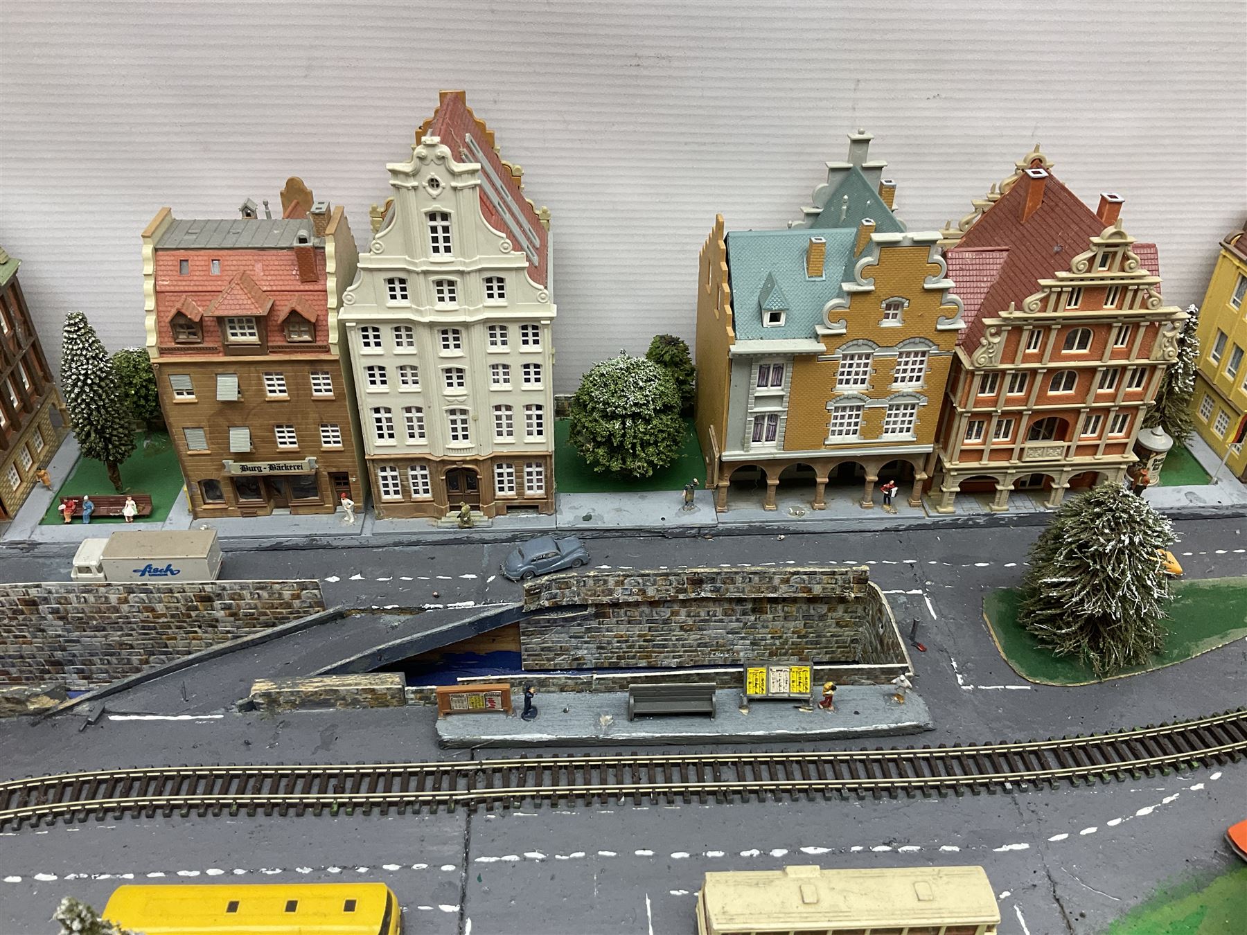 Table top 'N' gauge continental scenic layout as a split level town with various loops of track, station with numerous platforms, engine shed, assorted buildings, roads with motor vehicles and figures, tunnels, trees, river with bridge, tram depot etc 122 x 52cm
