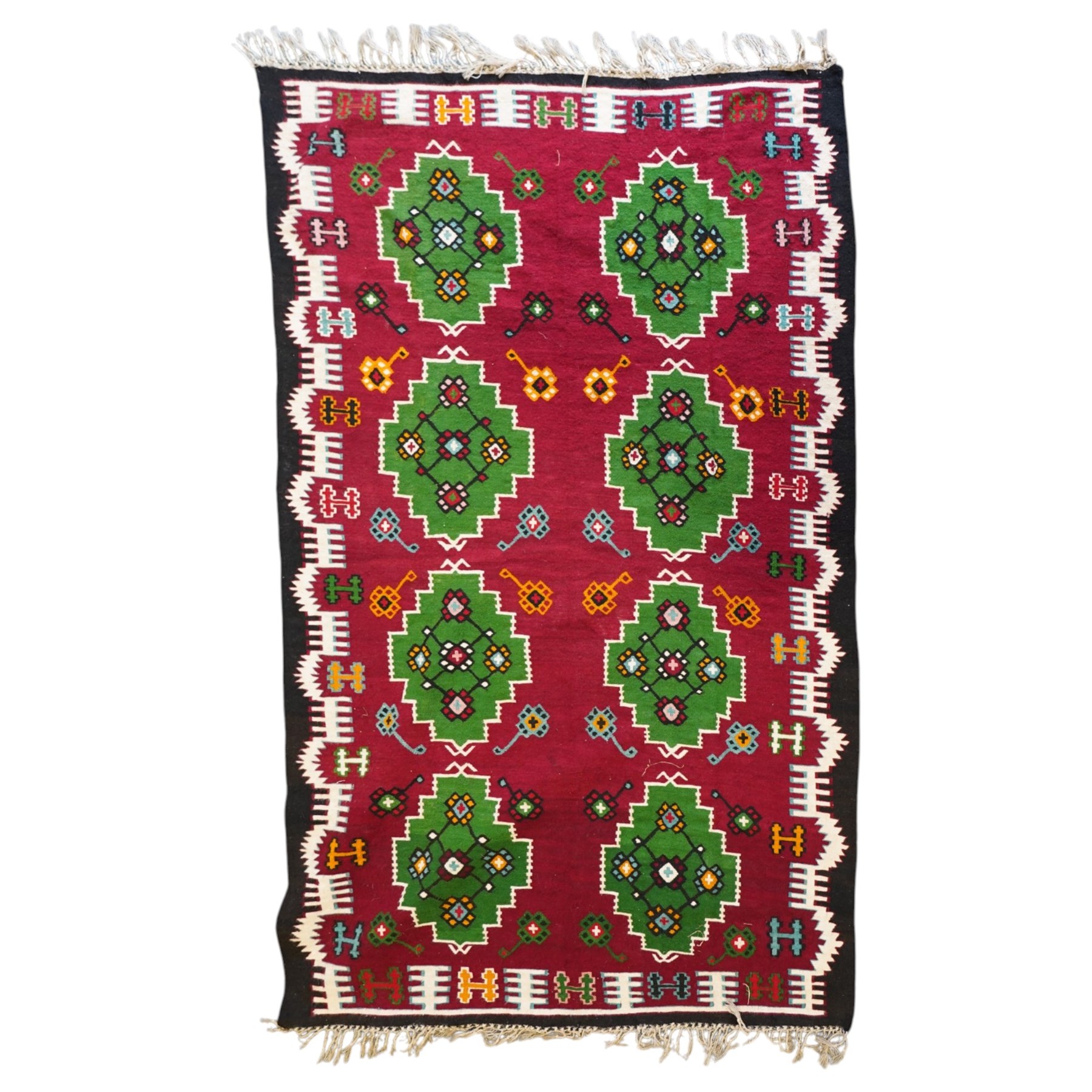 Persian Fars province crimson ground kilim rug, decorated with two rows of geometric emerald green motifs containing stylised plant designs, enclosed by an ivory and dark indigo guard band