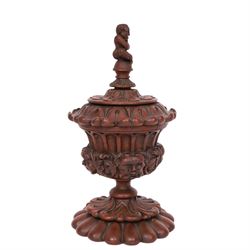 Carved wooden urn. decorated in relief with carved faces within foliage, with a Satyr finial, H25cm 