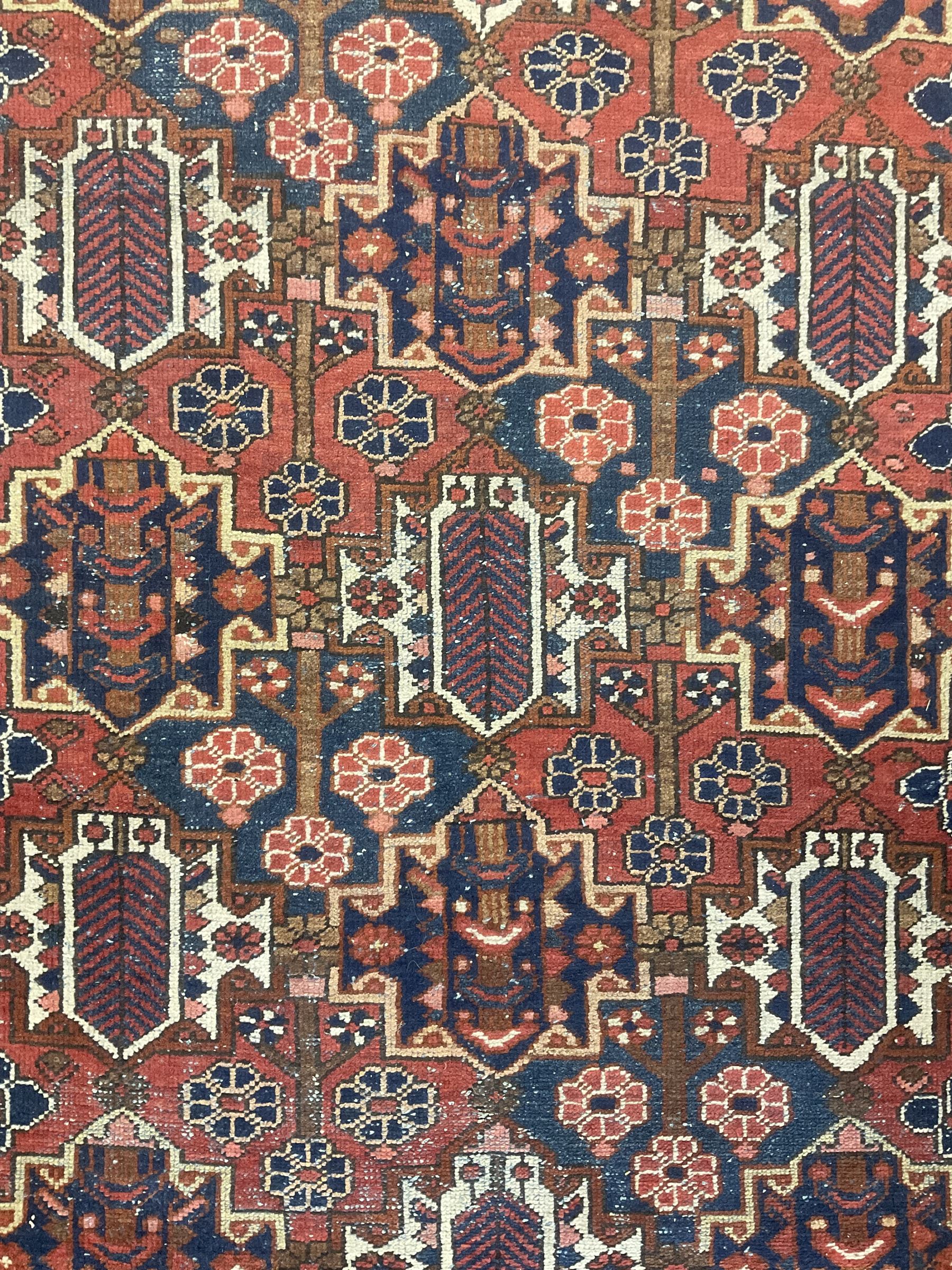 Persian crimson ground rug, the field decorated with three rows of stylised plant medallions and small flowerhead motifs, repeating floral design border with guards 