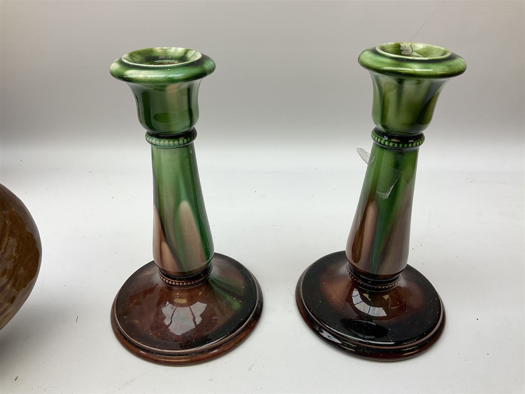 Linthorpe pottery vase with crimped rim and ovoid body, Linthorpe jug with high loop handle and crimped spout, a pair of candlesticks with a green, brown glaze and other similar pottery 