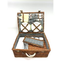 A wicker picnic hamper with accompanying contents. 