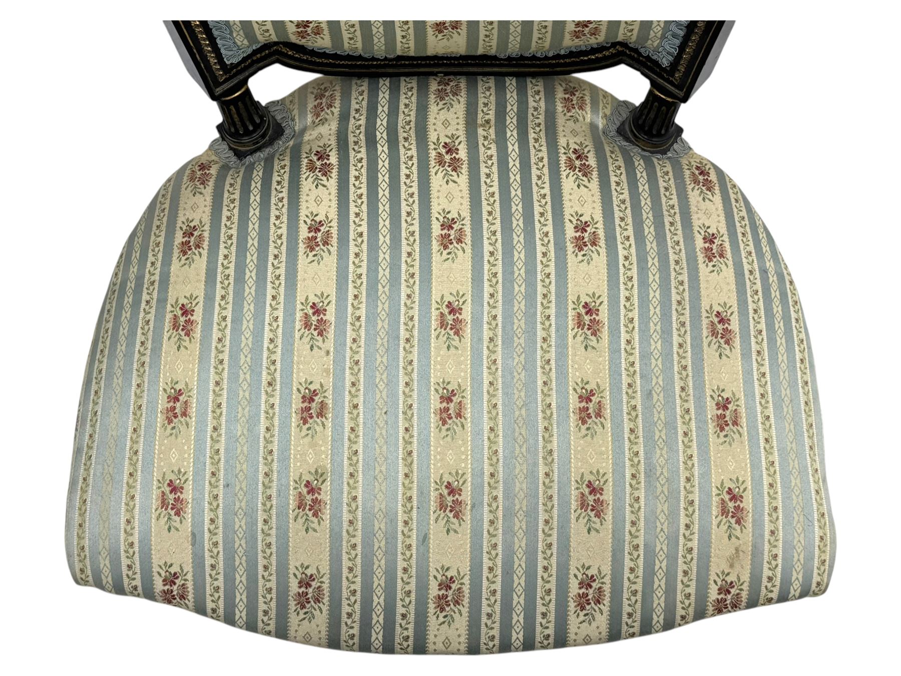 19th century French ebonised low chair, upholstered in floral striped fabric within a moulded frame with gilt line and foliate decoration, the seat of serpentine form, raised on turned fluted legs with toupie feet