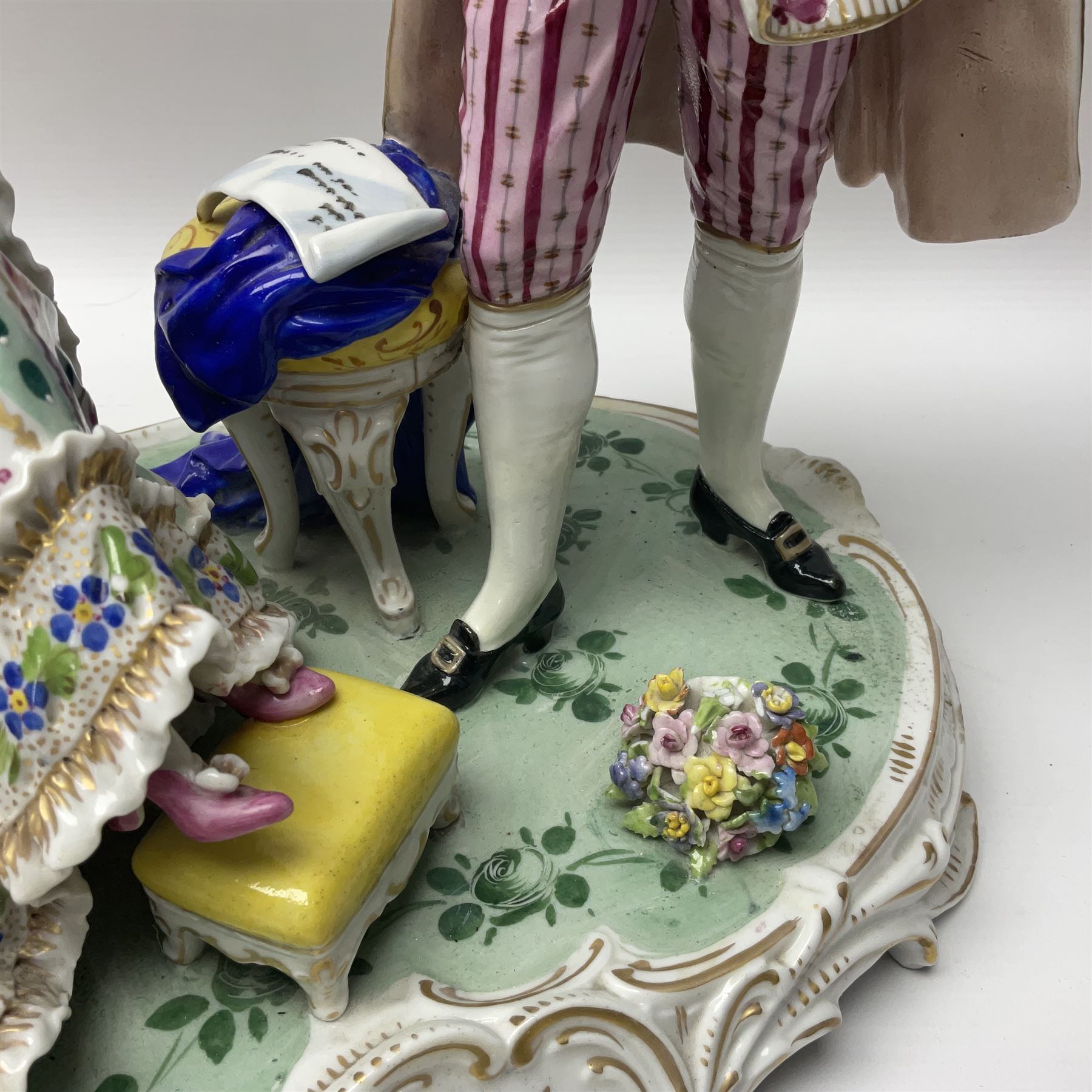 20th century Naples figure group, modelled as a seated female figure playing the lute seated, before a male figure stood holding a sheet of music, each in period dress, upon an oval base with gilt heightened scroll edge, with crowned N mark beneath, H31.5cm L33cm
