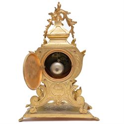 French-Late 19th century 8-day gilt brass rococo style mantel clock, c1890, waisted case  decorated with scroll work, leaves and musical instruments, resting on an attached plinth with splayed feet, dial within a glazed brass bezel with a gilt repoussé centre, porcelain cartouche Roman numerals and steel fleur-di-Lis hands, with a twin train movement, recoil anchor escapement and countwheel strike, sounding the hours and half-hours on a bell. With a matching pair of five-light candelabra. No Pendulum or Key.