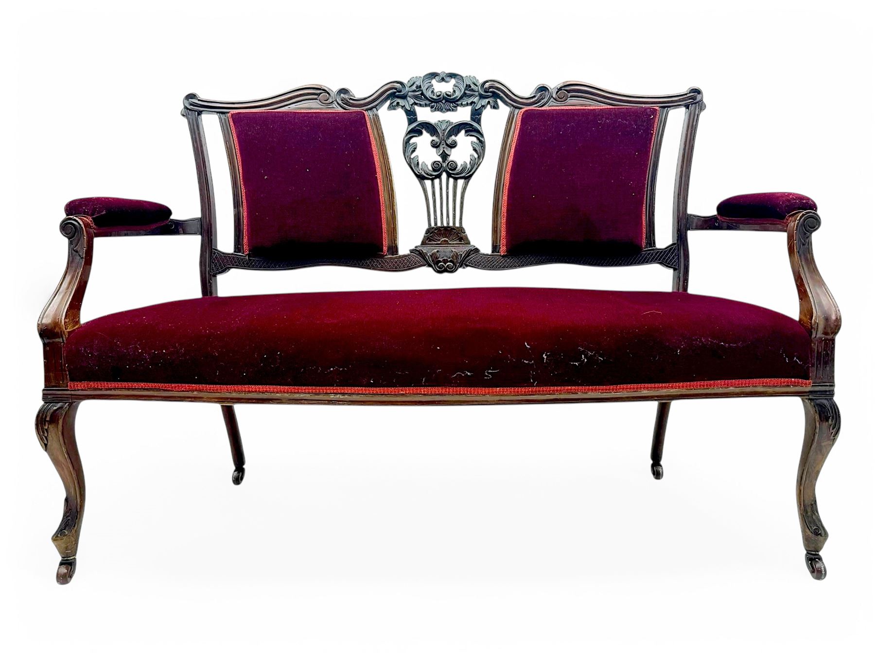 Late Victorian stained beech framed sofa, the backrests, seat and padded arms upholstered in deep red fabric, carved crest rail with scroll and foliate motifs supported by carved uprights, on cabriole supports with leaf carvings terminating in castors