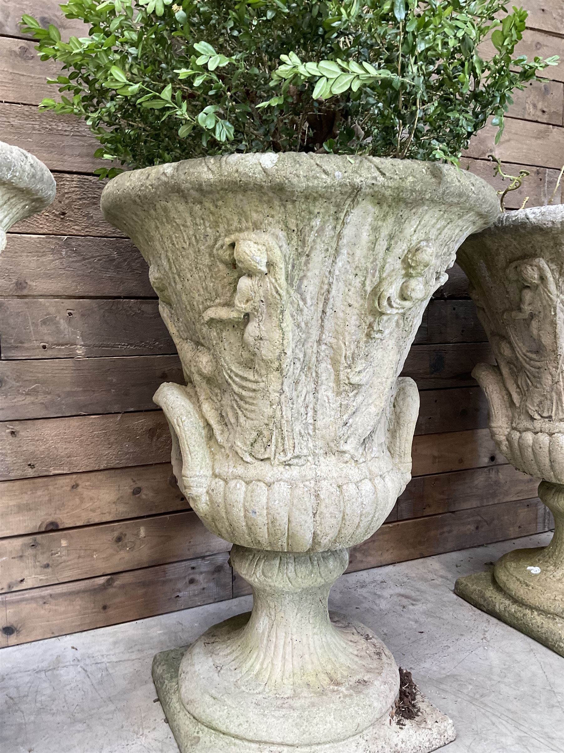 Set of four Victorian design cast stone Grecian urns, tapering form cast with figures and handles, square plinth bases