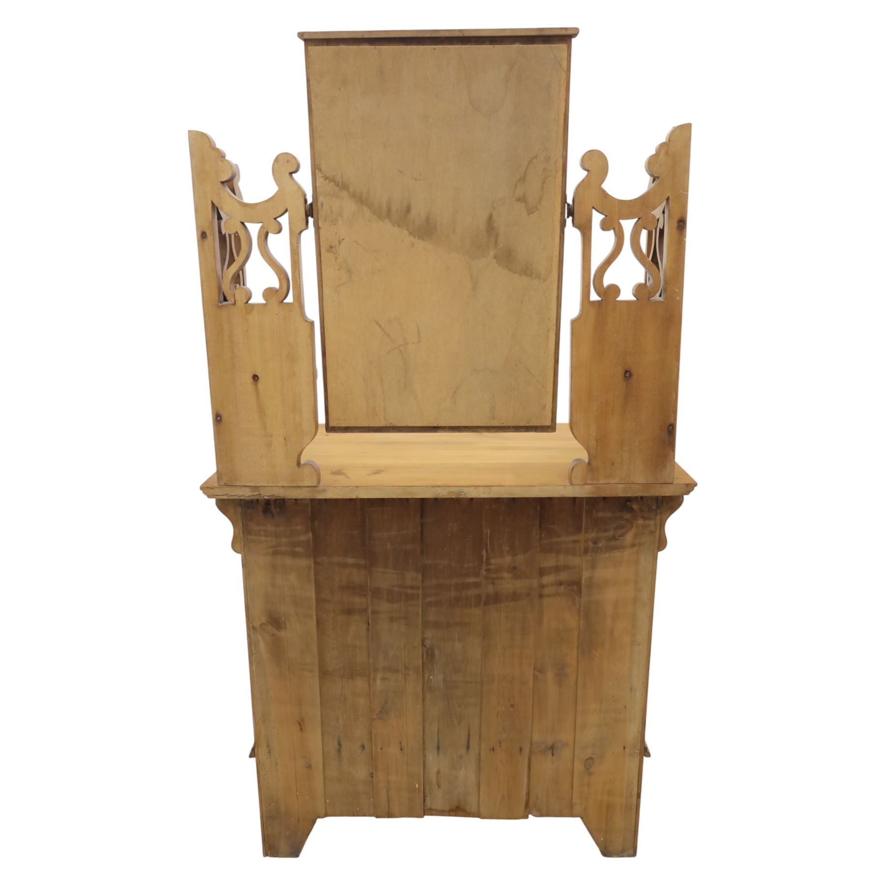 Edwardian stained pine dressing chest, the moulded top over three graduating drawers with pressed brass handles, shaped apron and bracket feet, the mirror back with rectangular plate on pivot supports, flanked by pierced Gothic style uprights with small corner shelves