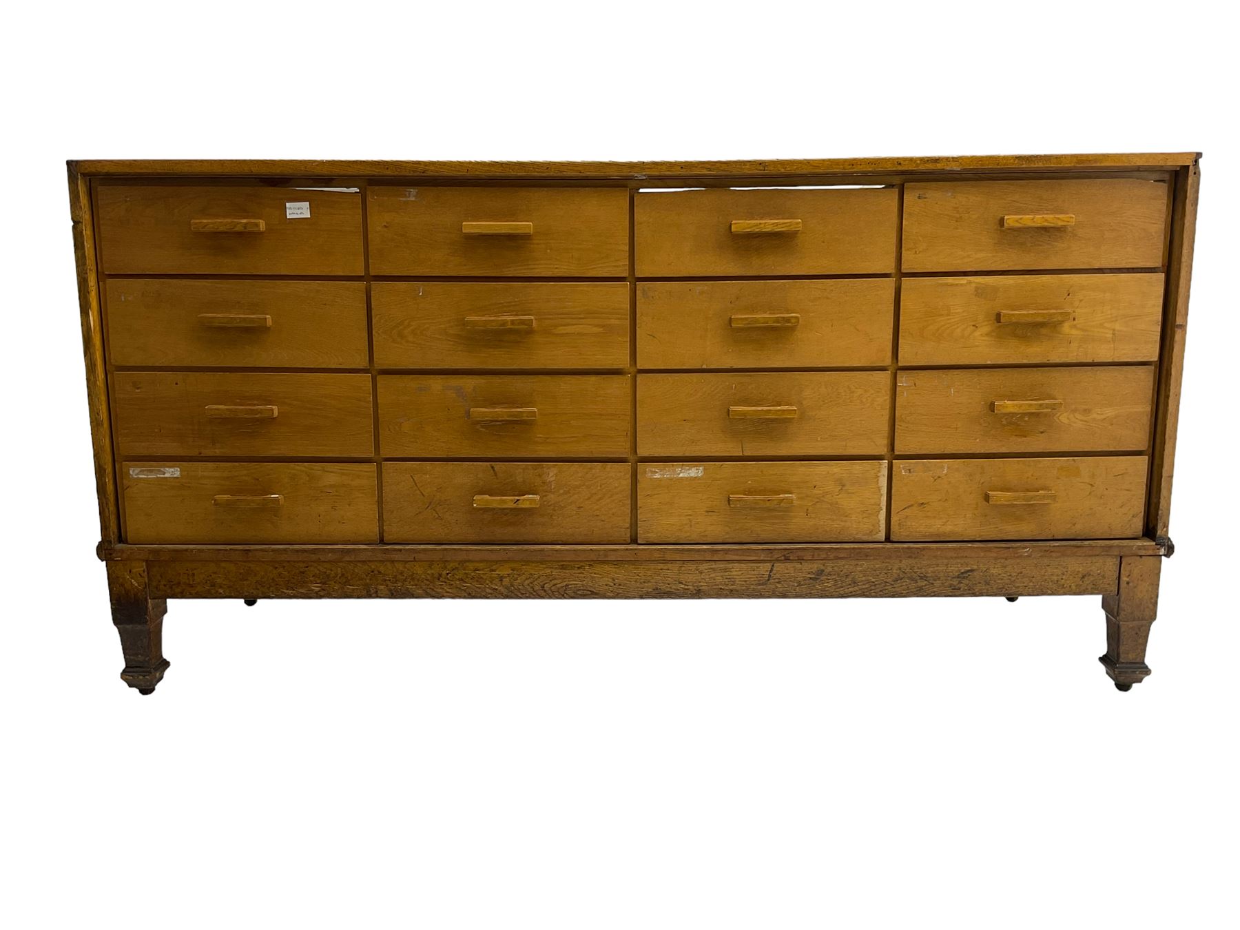 Early 20th century oak framed haberdashery shop counter, glass panel exterior enclosing sixteen graduating drawers with oak fronts and handles, raised on shaped tapering supports 