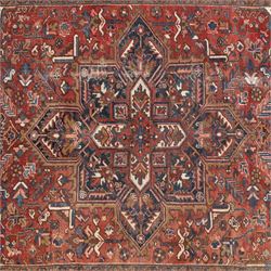Persian Heriz carpet, red ground with large central geometric medallion, angular flowering branches and stylised foliate decoration, within a broad dark blue floral border and narrow guard stripes