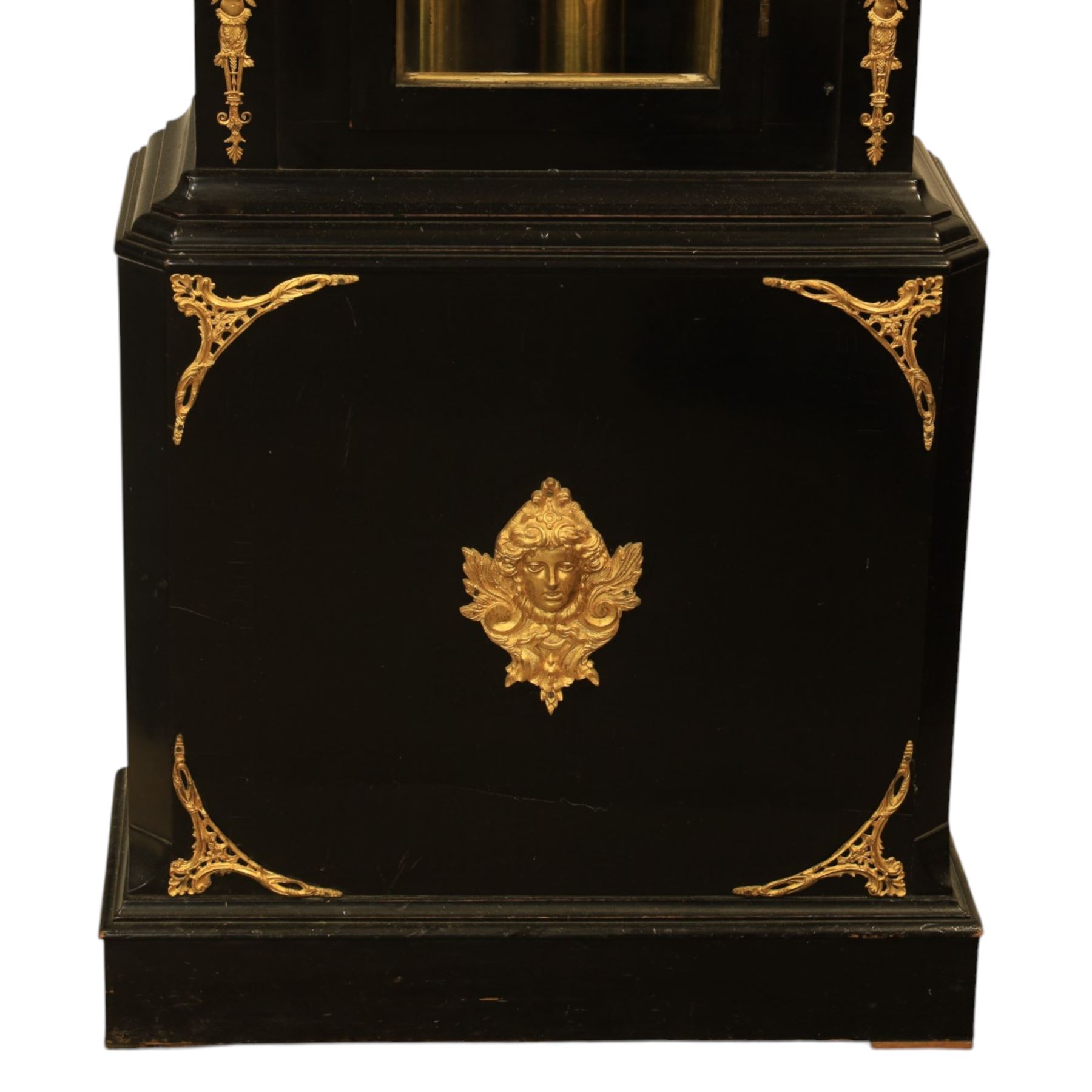 Late nineteenth century ebonised and gilt-bronze mounted musical longcase clock of impressive architectural form, the case of ebonised finish with applied gilt bronze neoclassical inspired masks and mounts, hood of arched form with glazed door, flanked by free fluted columns with gilt bronze Corinthian capitals surmounted by stylized Lion finials, frieze and arch enriched with applied foliate mounts, trunk with a rectangular glazed door bordered by mouldings and flanked by engaged columns with gilt bronze mounts above a shaped projecting base panel with applied central female mask and corner foliate ornamentation, arched brass dial, with a silvered chapter ring and applied cast gilt bronze spandrels and arch decoration, incorporating subsidiary selection dials for chime/silent and tune regulation, offering Cambridge chimes on eight bells and an additional chime sequence on ten bells, brass arch is further embellished with a moon phase aperture with lunar calendar scale, Zodiac symbols, month and date indication on a silvered dial, substantial eight-day, three-train movement with pinned cylinder musical train and a graduated nest of eleven bells with eleven hammers, quarter chiming with separate hour/half-hour strike and chime repetition, movement is regulated by an anchor escapement, with brass disc pendulum, three brass weights, two winding keys and case door key
