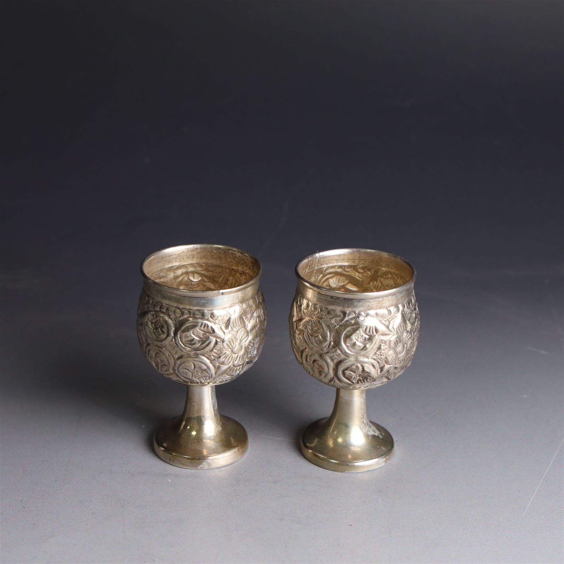 Pair of miniature Indian silver goblets, with embossed floral and foliate decoration, H6.5cm