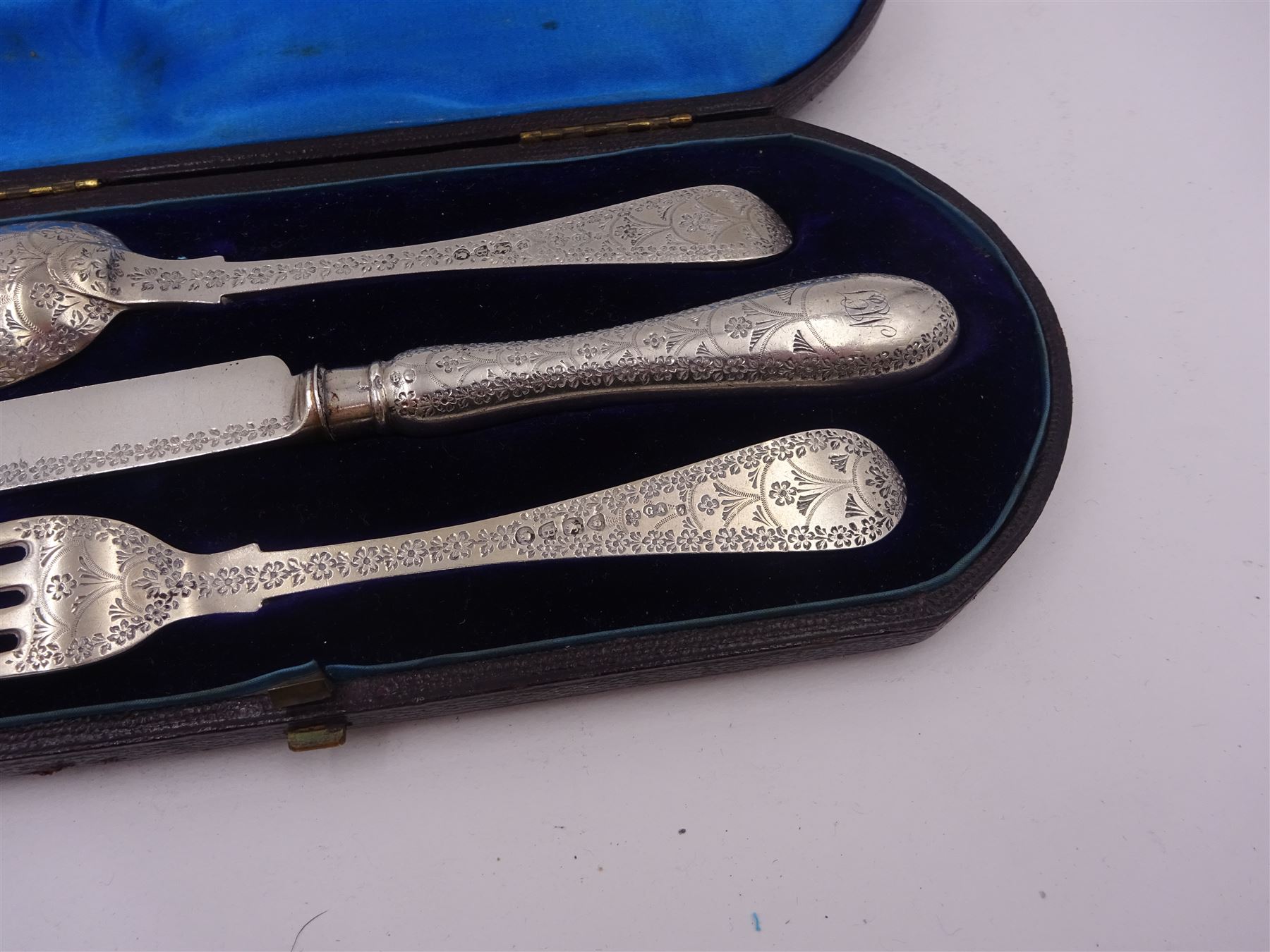 Victorian silver cutlery set, comprising knife, fork and spoon, all profusely engraved with flower heads, each with initials terminals, hallmarked Chawner & Co Birmingham 1877, contained within tooled leather, velvet and silk lined fitted case