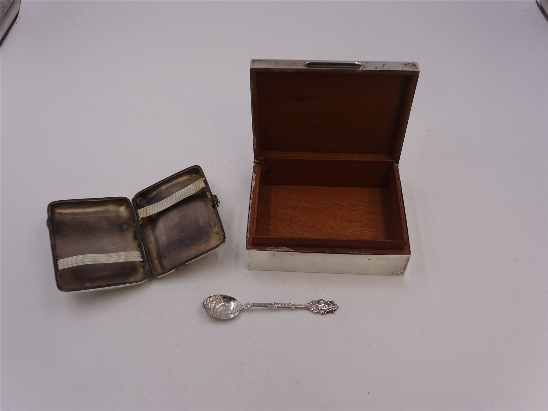 Modern silver mounted cigarette box, of plain rectangular form, with personal engraving to hinged cover, opening to reveal soft wood lined interior, H3.8cm, W21.5cm, hallmarked Padgett & Braham Ltd, London 1967, together with a silver cigarette case, with engraved C scroll decoration, hallmarked Joseph Gloster Ltd, Birmingham 1917 or 1942 and a silver souvenir spoon