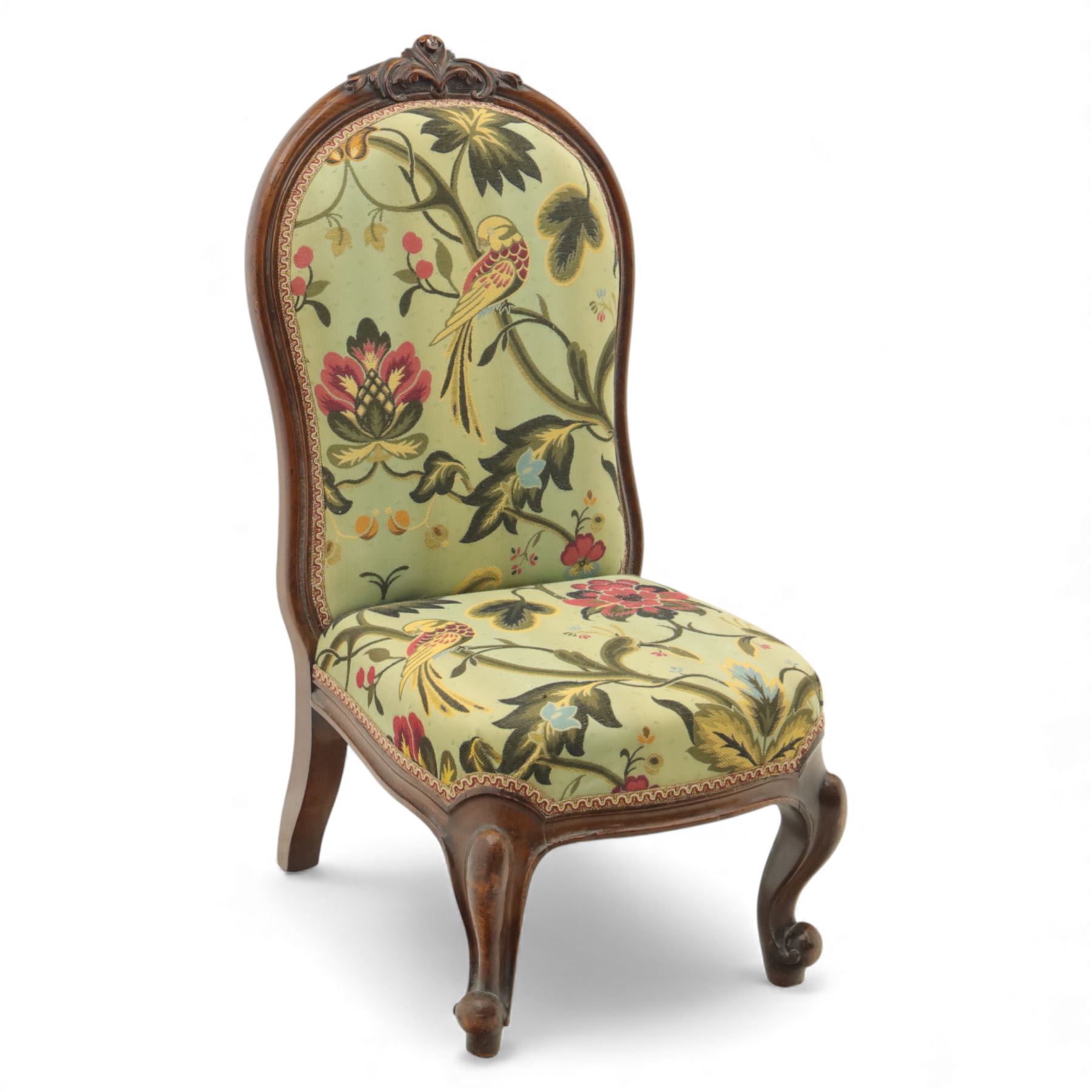Small Victorian mahogany nursing chair, with carved top rail above a padded balloon back and shaped seat upholstered in light green fabric detailed with exotic birds and flowering vines, raised upon cabriole front legs and turned rear supports