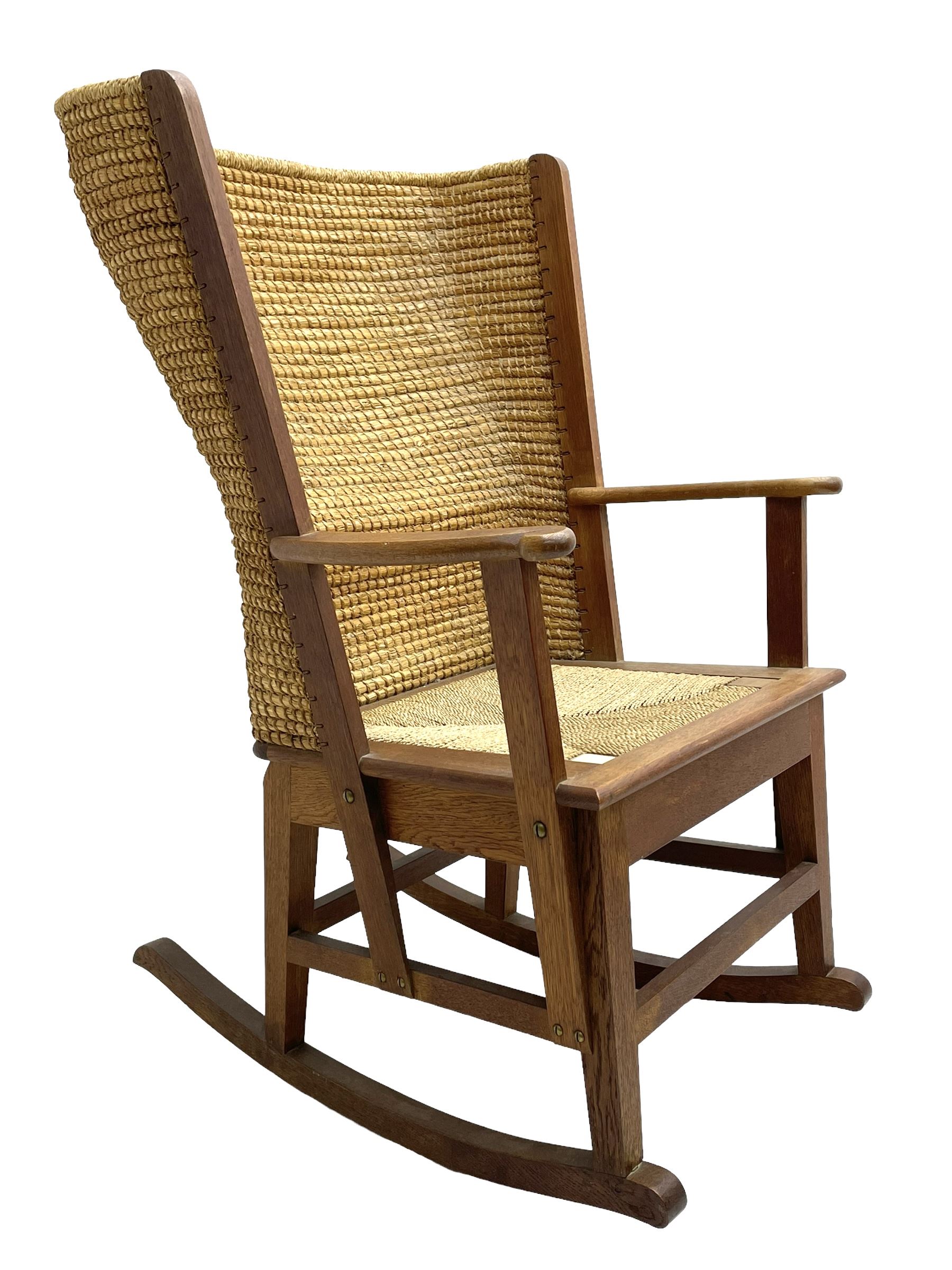 Reynold Eunson (1932–1978) for David Munro Kirkness, Kirkwall, Orkney - oak framed Orkney rocking chair, woven straw curved back, drop-in rush seat, the arm terminals with carved end scroll, on square tapering supports joined by plain stretchers, the front rail inscribed with makers marks