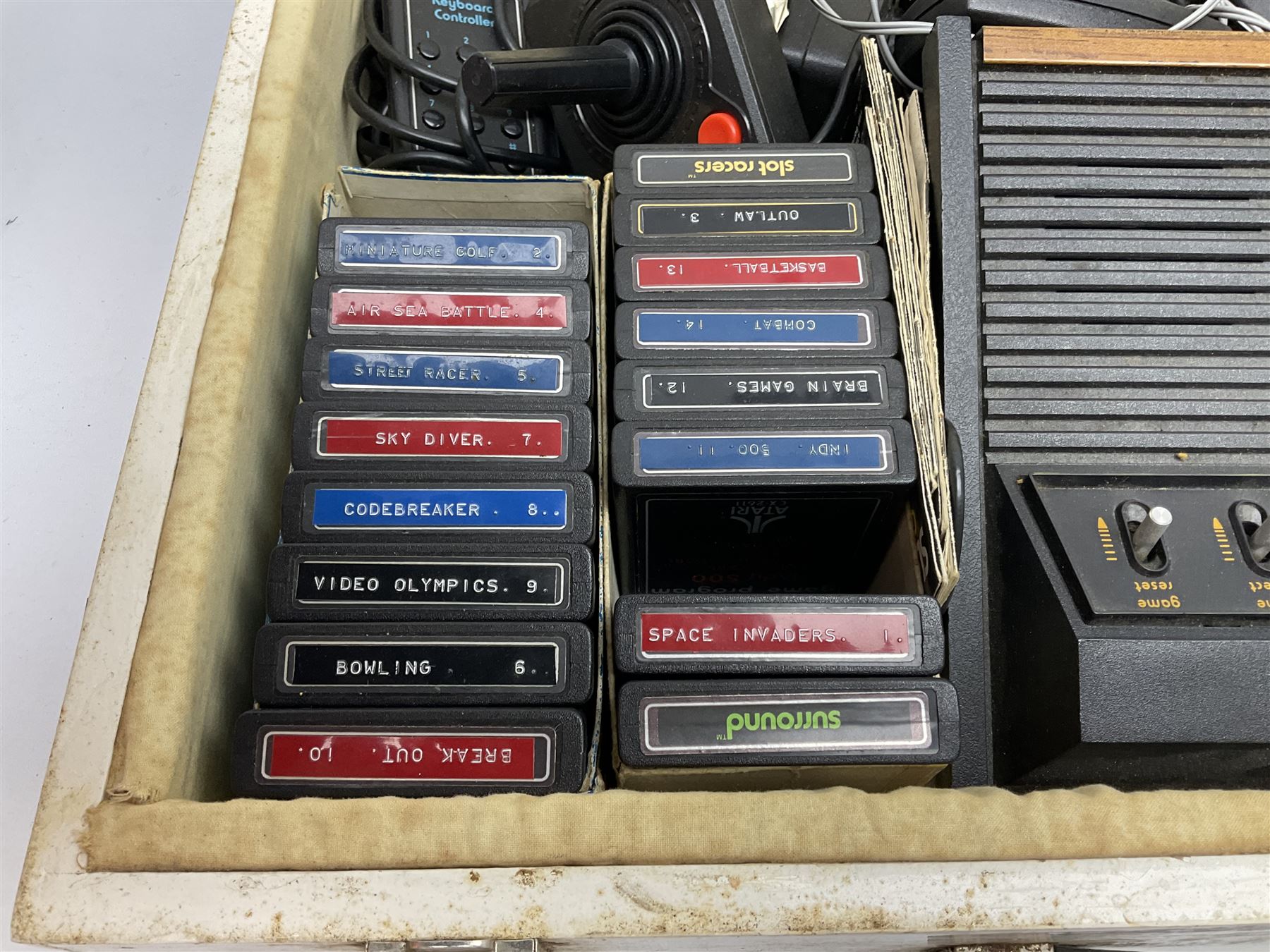 Atari 2600 'Woody' console with various joysticks and controllers etc, and a quantity of game cassettes to include 'Outlaw', 'Air Sea Seattle' and 'Codebreaker' etc housed in white painted wood case
