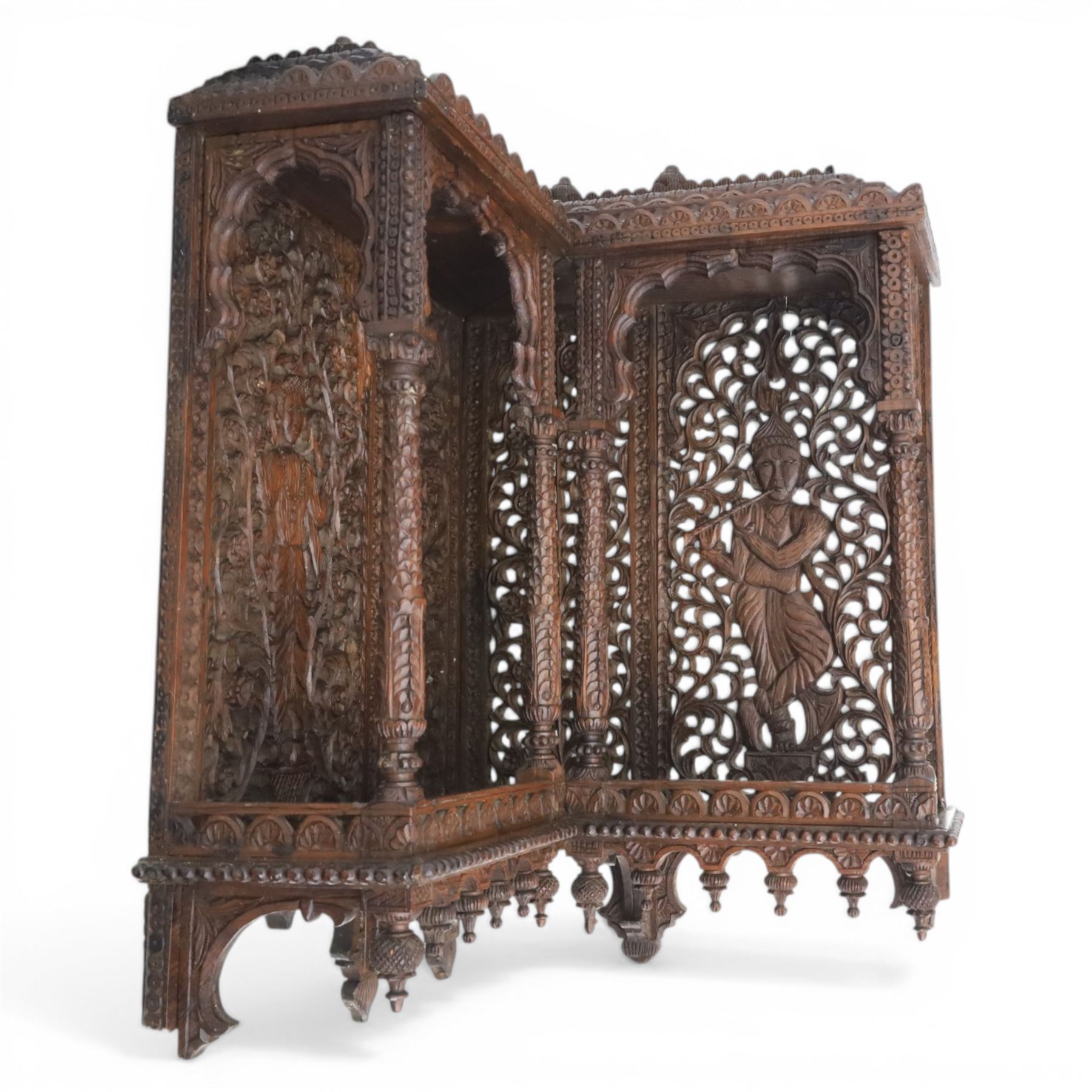 20th century Indian carved hardwood corner shelf, the tiered pagoda form with pierced and carved foliate panels centred by figural carving, supported by turned and carved columns, with shaped brackets and pendant finials