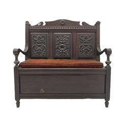 Late 19th century oak settle bench, shaped cresting rail carved with ribbon over triple panelled back, the panels relief carved with scrolled and floral urns and cartouche, hinged box seat, turned front feet, with upholstered squab cushion