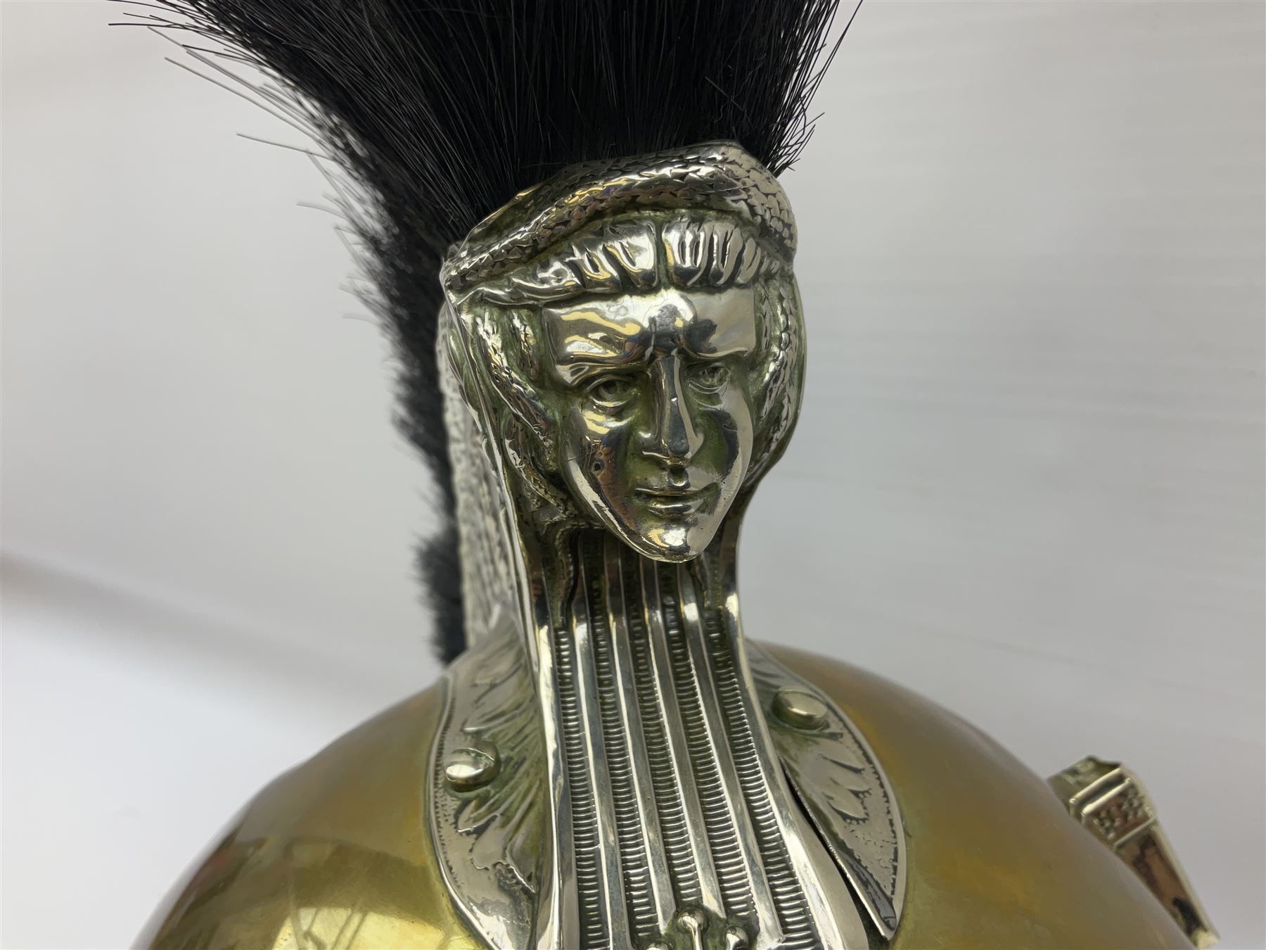 Early 20th century French mounted gendarme's helmet, brass with nickel-silver mountings, broad band embossed with fused grenade, high comb with the face of the gorgon Medusa at the peak and with a black horse hair crest, plume socket at the left, leather-backed nickel-silver chin scales with lion mask mounts.