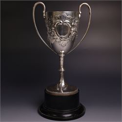 Edwardian silver twin-handled trophy, with embossed floral and scrolling decoration, upon a knopped stem and circular foot, hallmarked Goldsmiths & Silversmiths Co Ltd, London 1903, upon a black plinth, including plinth and handles H32cm