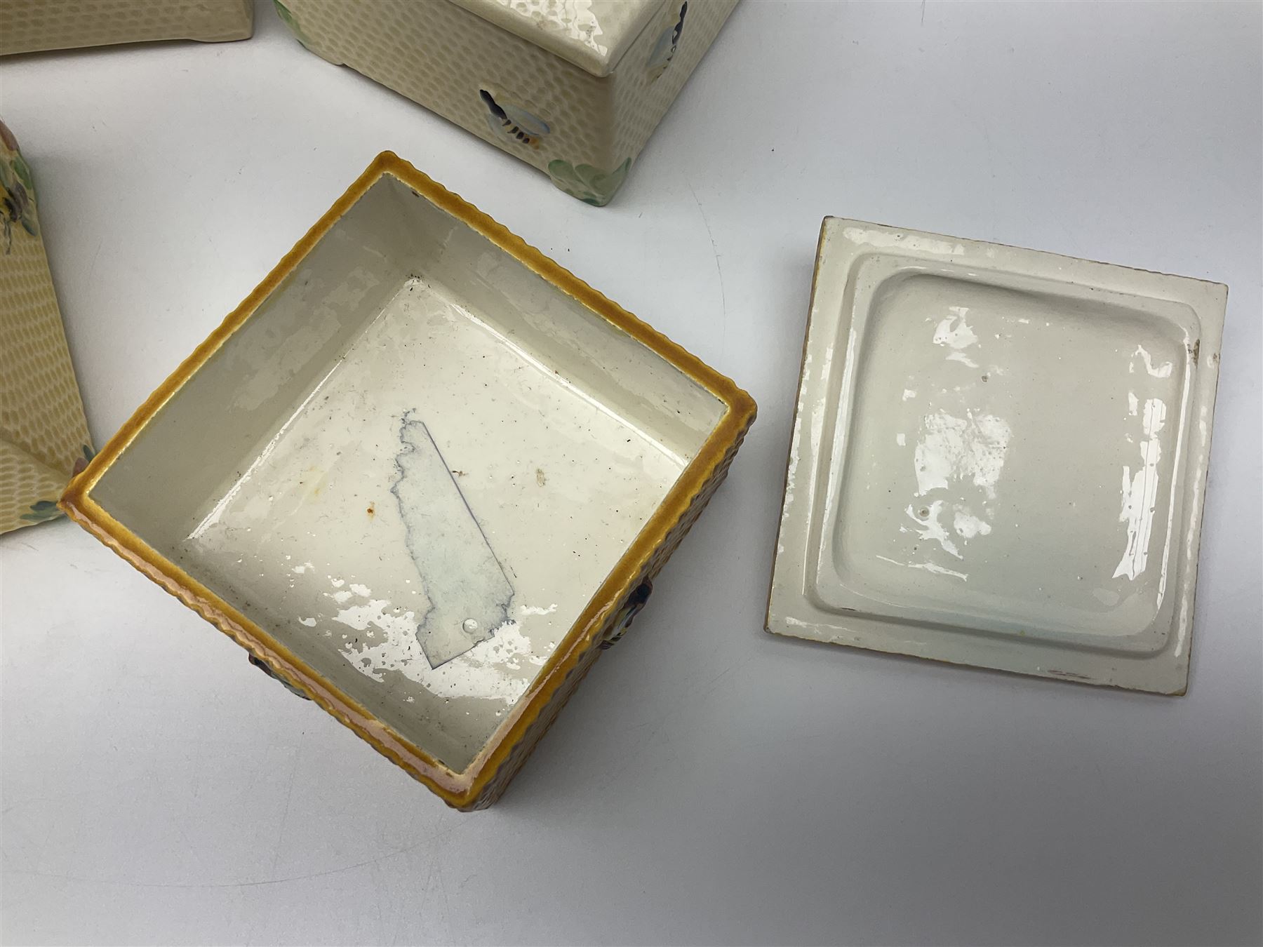 Four square honey boxes with lids,  each decorated with honeycomb pattern and finished with a bee finial